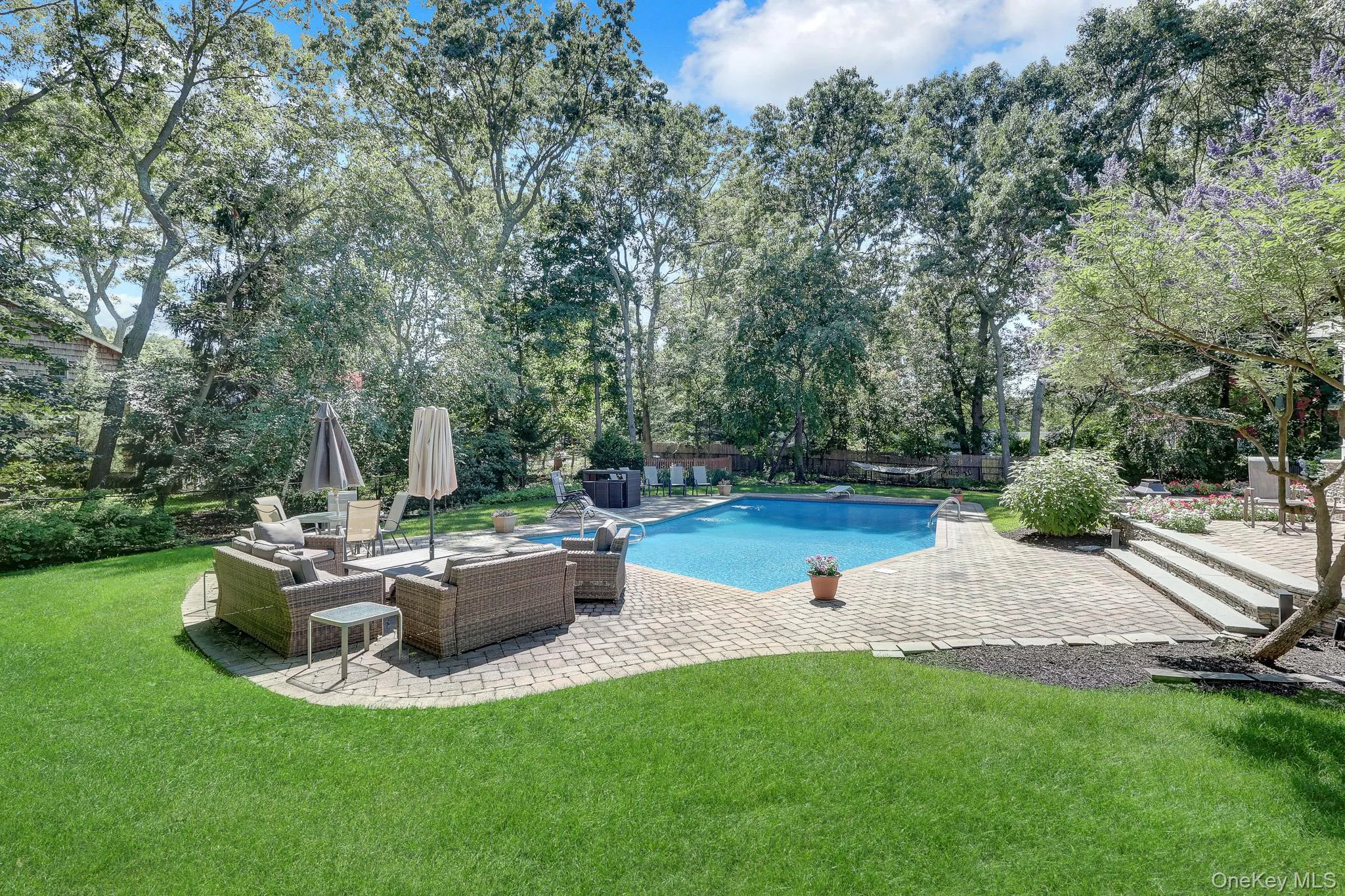 Expansive backyard featuring a swimming pool with a surrounding paver patio, stone steps, and a lush lawn Expansive backyard featuring a swimming pool with a surrounding paver patio, stone steps, and a lush lawn