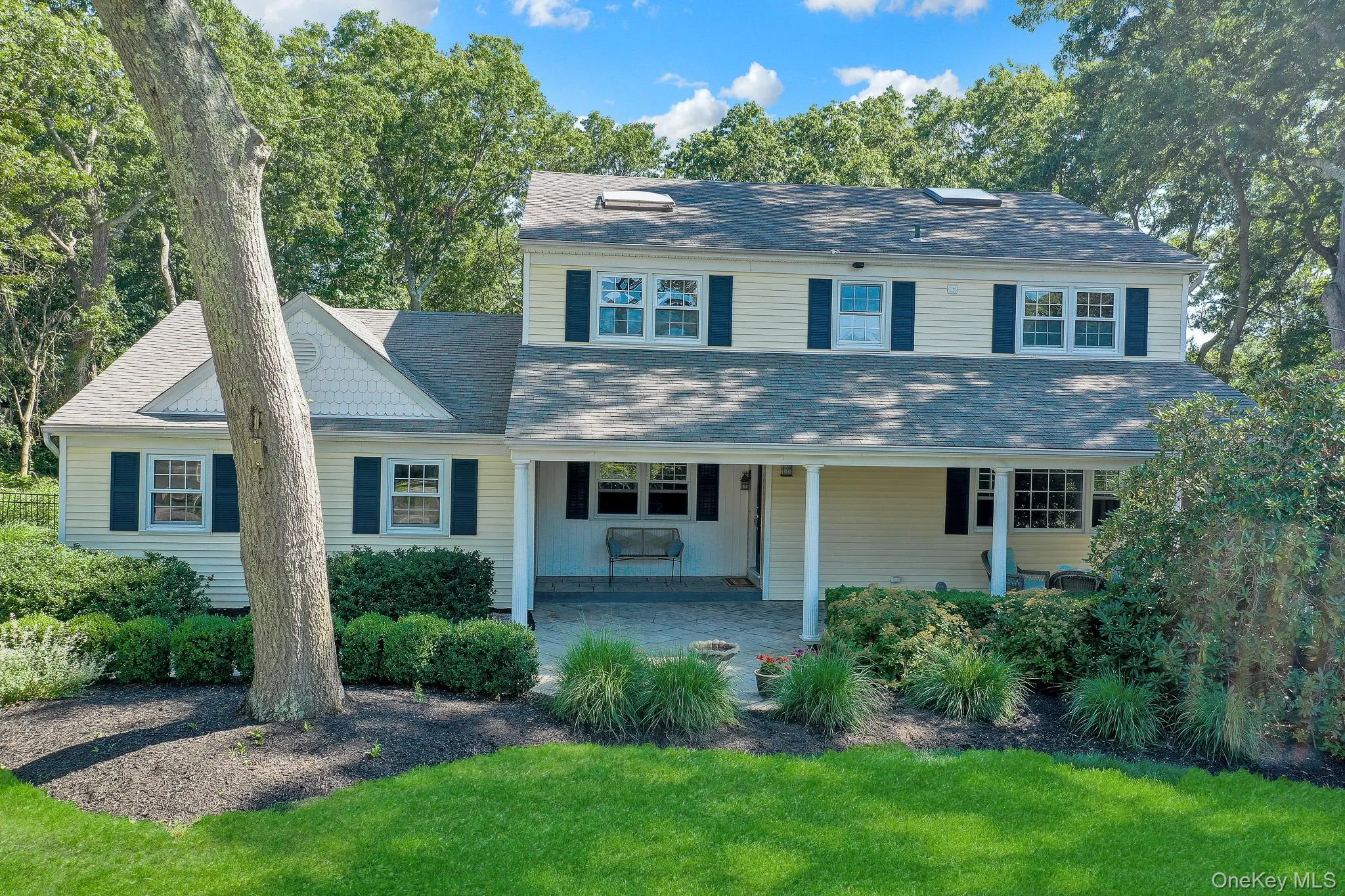 Traditional-style home featuring light-colored siding, dark shutters, and an extended covered front porch with a paver patio Traditional-style home featuring light-colored siding, dark shutters, and an extended covered front porch with a paver patio