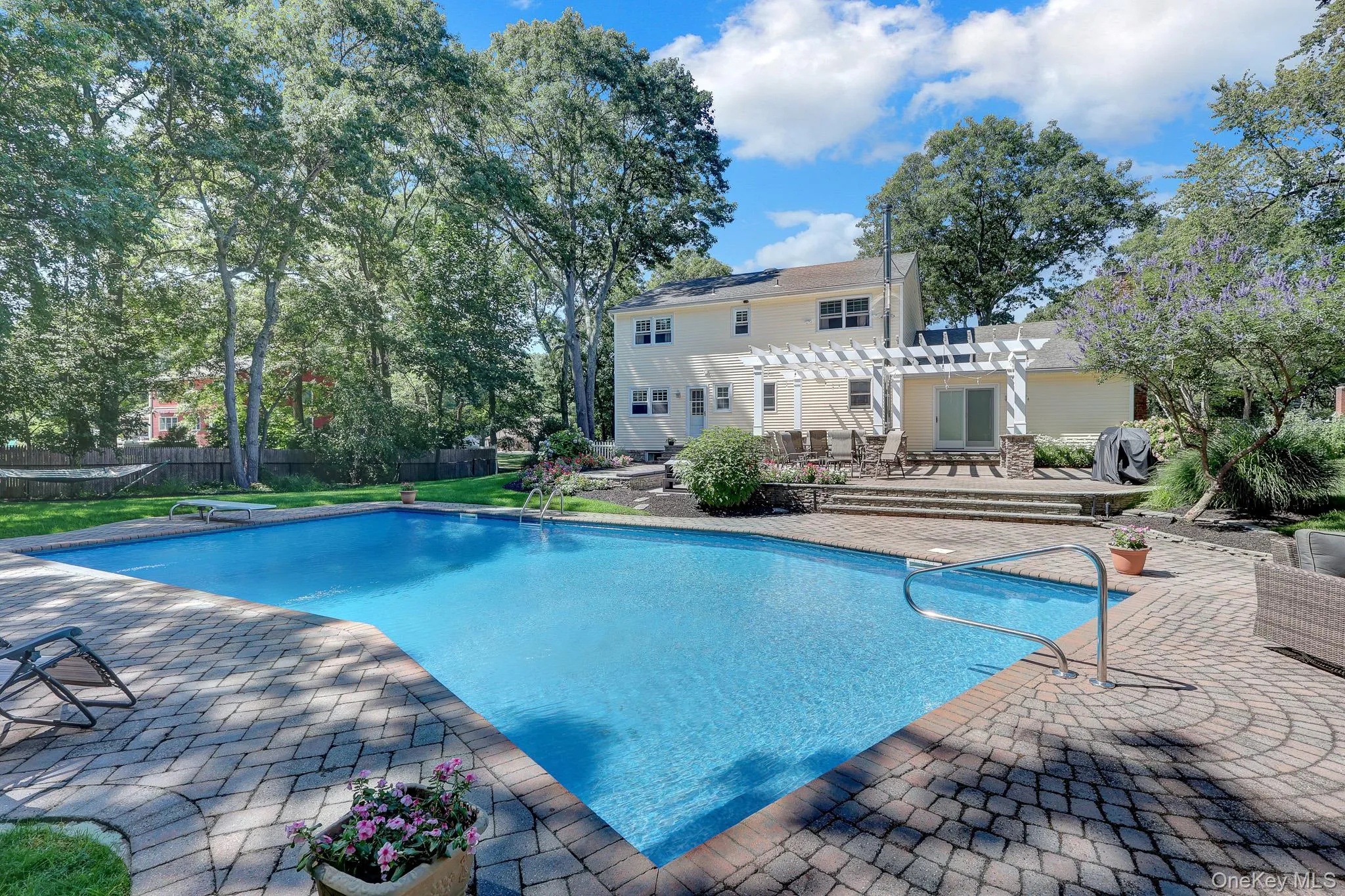 Expansive outdoor living area featuring a rectangular swimming pool, brick paver patio, and a pergola-covered patio with a sliding glass door Expansive outdoor living area featuring a rectangular swimming pool, brick paver patio, and a pergola-covered patio with a sliding glass door