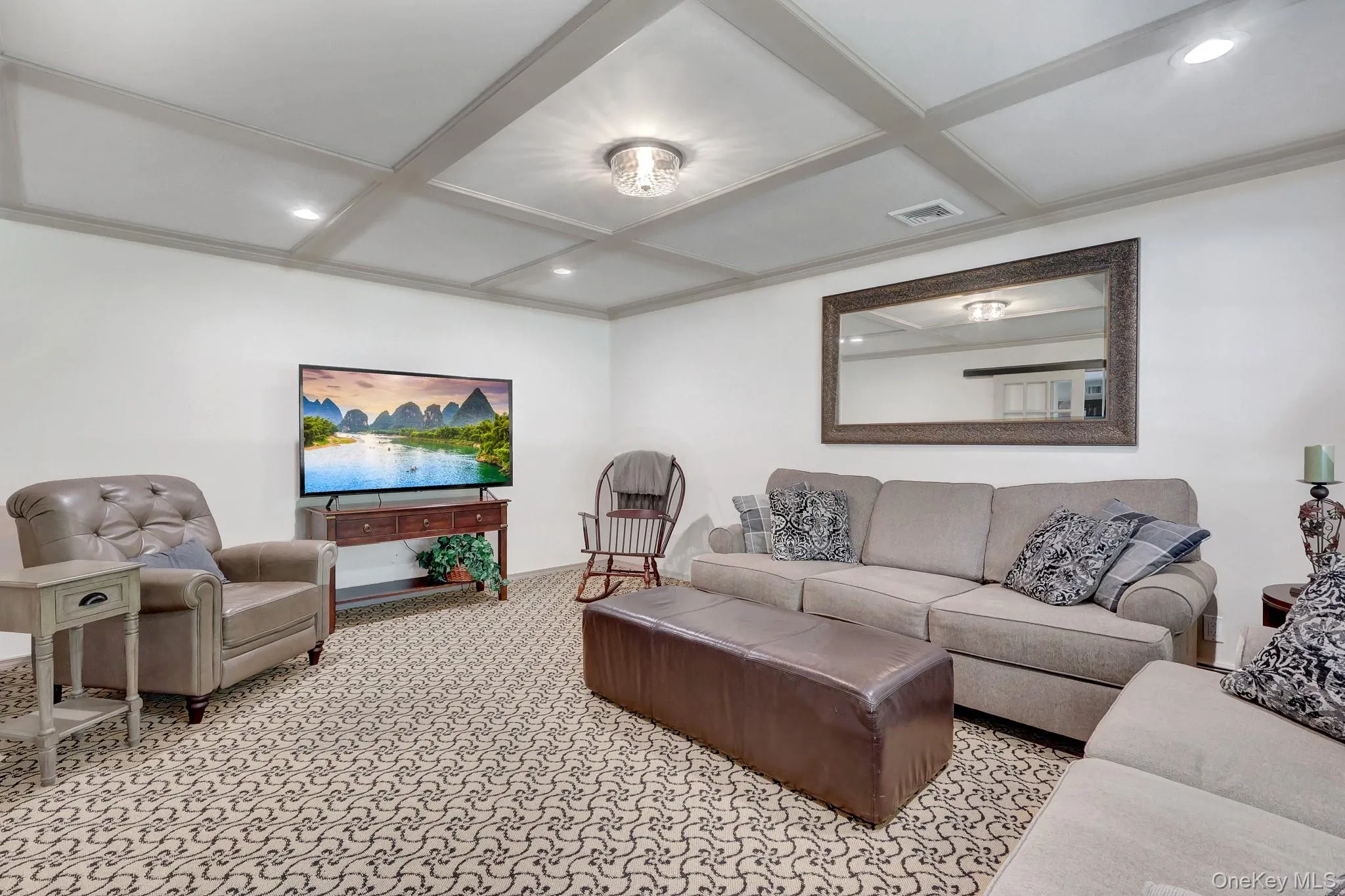 Living area featuring a coffered ceiling with recessed lighting, patterned carpet flooring, and a large wall-mounted mirror Living area featuring a coffered ceiling with recessed lighting, patterned carpet flooring, and a large wall-mounted mirror