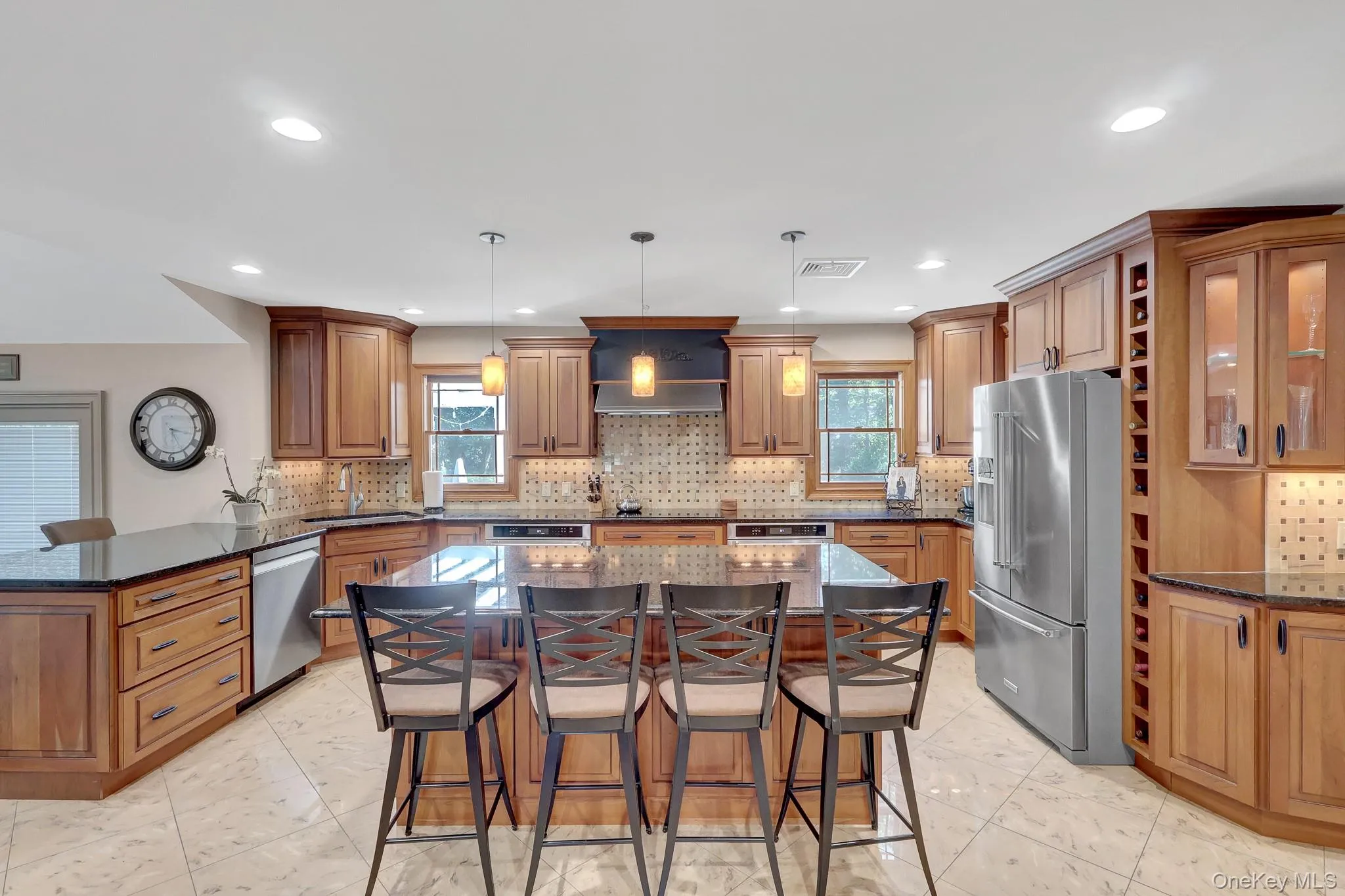 Spacious kitchen featuring an expansive center island with seating, warm wood cabinetry, built in wine rack, dark countertops, stainless steel appliances, and tile flooring Spacious kitchen featuring an expansive center island with seating, warm wood cabinetry, built in wine rack, dark countertops, stainless steel appliances, and tile flooring