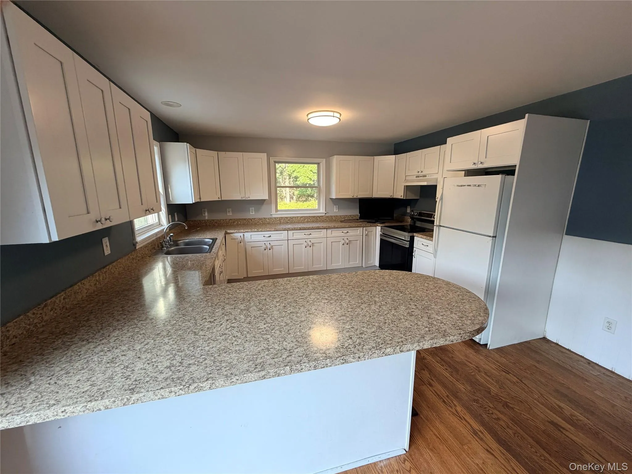 Kitchen featuring white cabinetry, speckled countertops, a double basin sink, and wood-finish flooring Kitchen featuring white cabinetry, speckled countertops, a double basin sink, and wood-finish flooring
