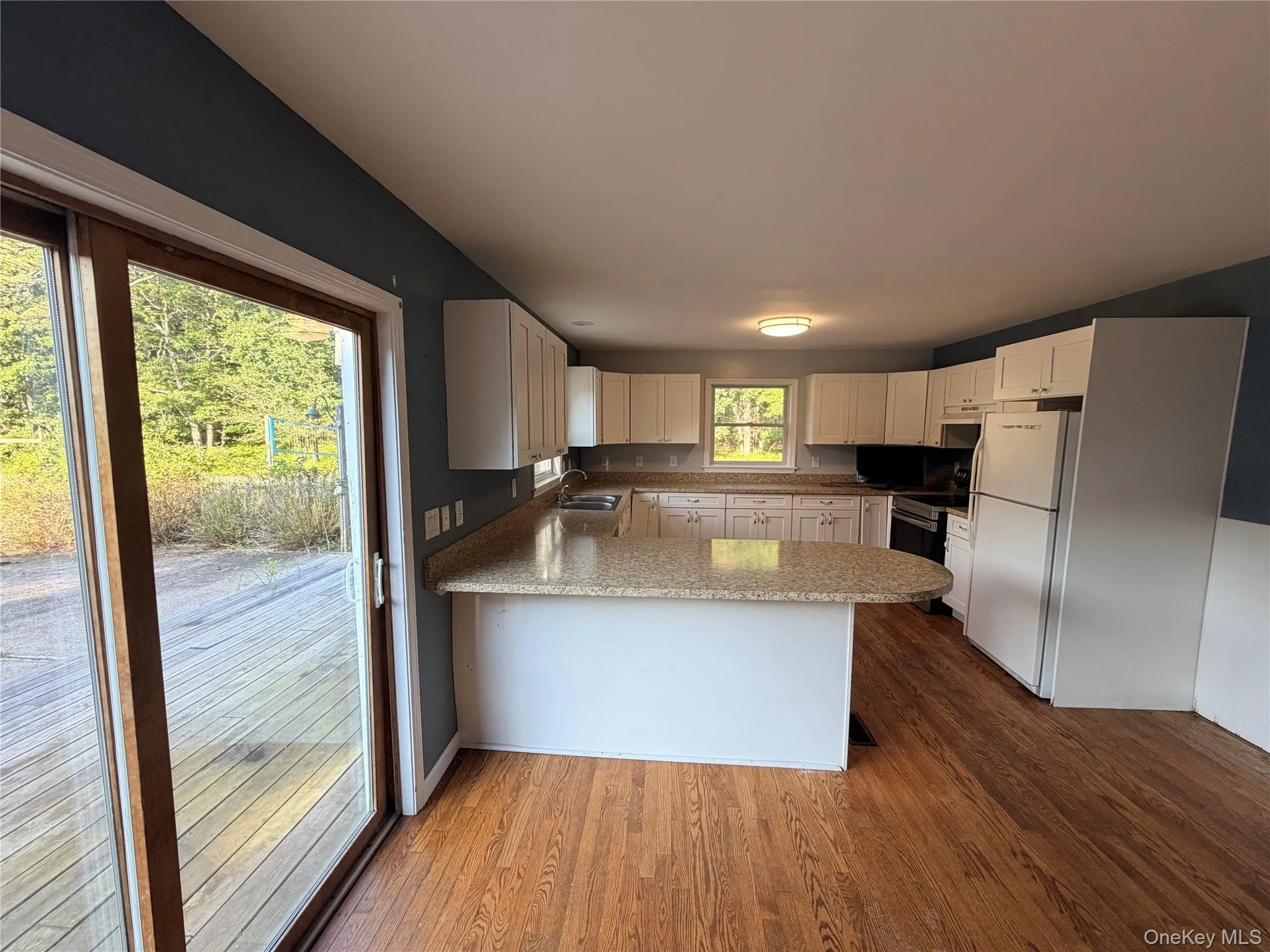 Kitchen featuring wood-finish flooring, white cabinetry, and light-colored countertops Kitchen featuring wood-finish flooring, white cabinetry, and light-colored countertops