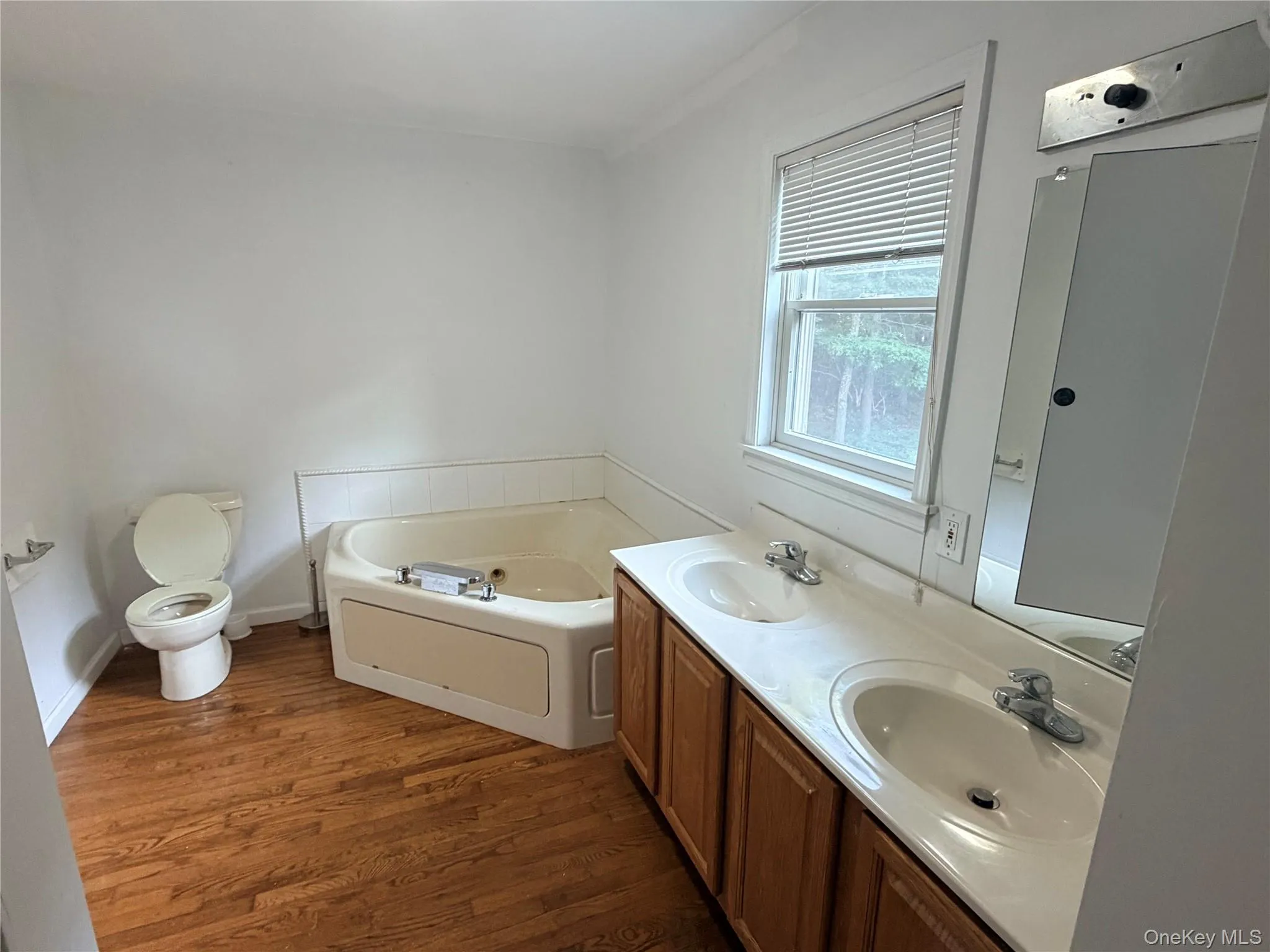 Spacious bathroom featuring wood-finish flooring and a corner soaking tub Spacious bathroom featuring wood-finish flooring and a corner soaking tub