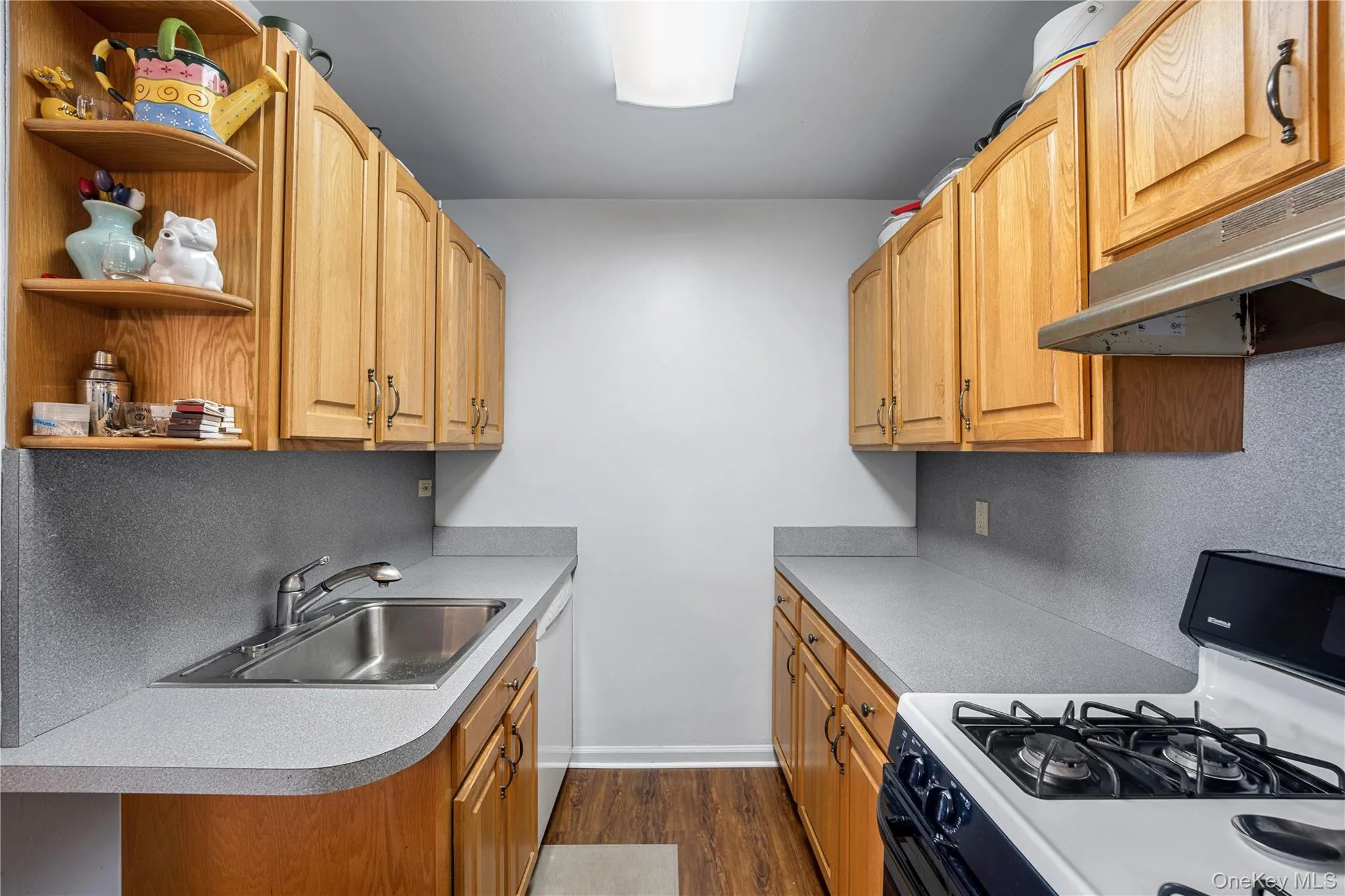 Galley kitchen featuring wood-finish cabinetry, light-toned countertops, and a stainless steel sink Galley kitchen featuring wood-finish cabinetry, light-toned countertops, and a stainless steel sink