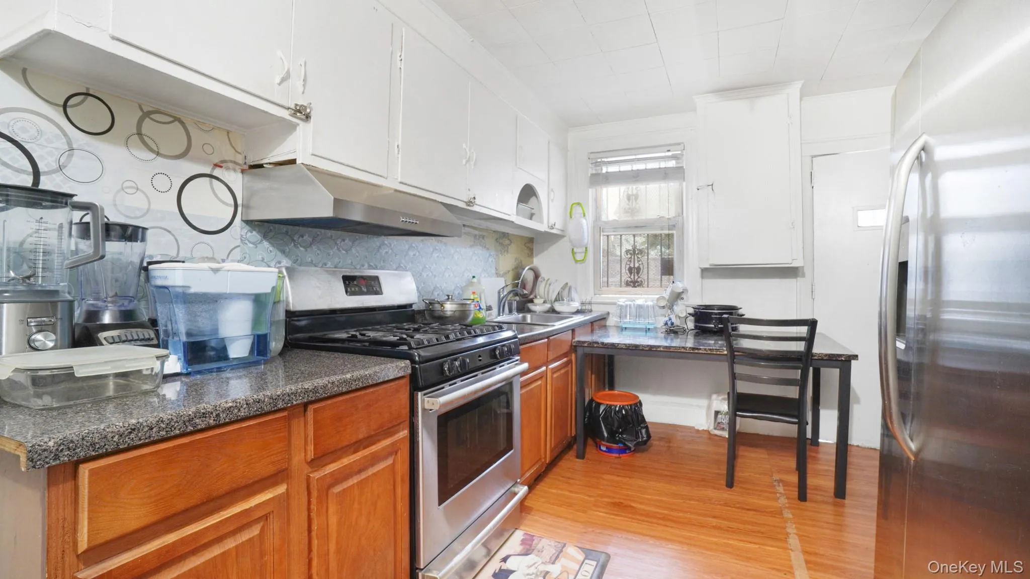 Kitchen featuring stainless steel appliances, under cabinet range hood, light wood finished floors, decorative backsplash, and brown cabinetry Kitchen featuring stainless steel appliances, under cabinet range hood, light wood finished floors, decorative backsplash, and brown cabinetry