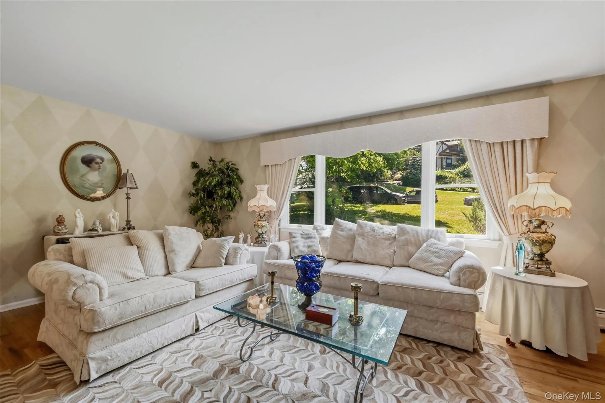 Bright interior space featuring a large picture window, patterned accent wall, hardwood flooring, and a decorative valance Bright interior space featuring a large picture window, patterned accent wall, hardwood flooring, and a decorative valance