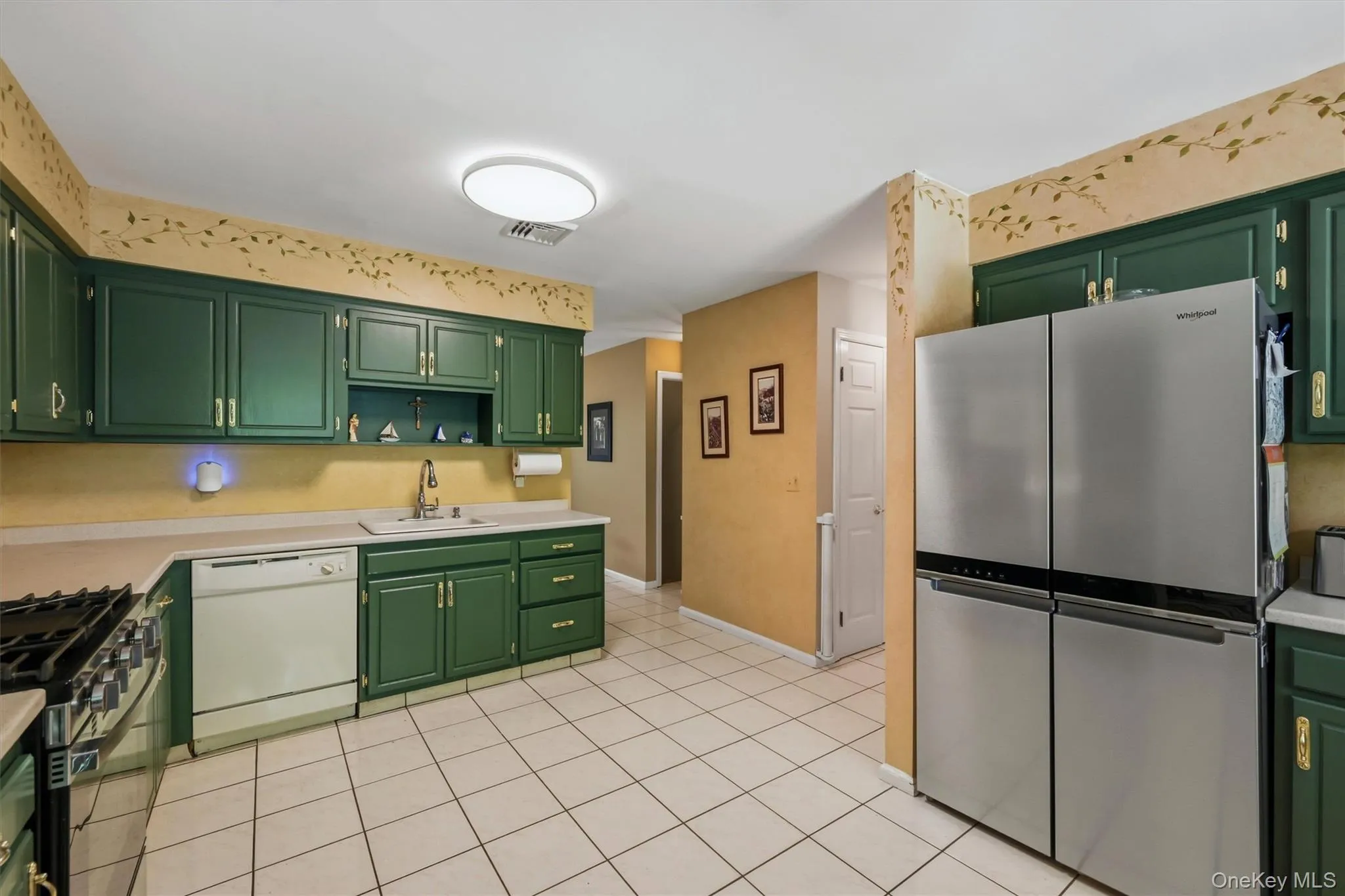 Kitchen featuring ample green cabinetry, stainless steel refrigerator, white dishwasher, and a gas range Kitchen featuring ample green cabinetry, stainless steel refrigerator, white dishwasher, and a gas range