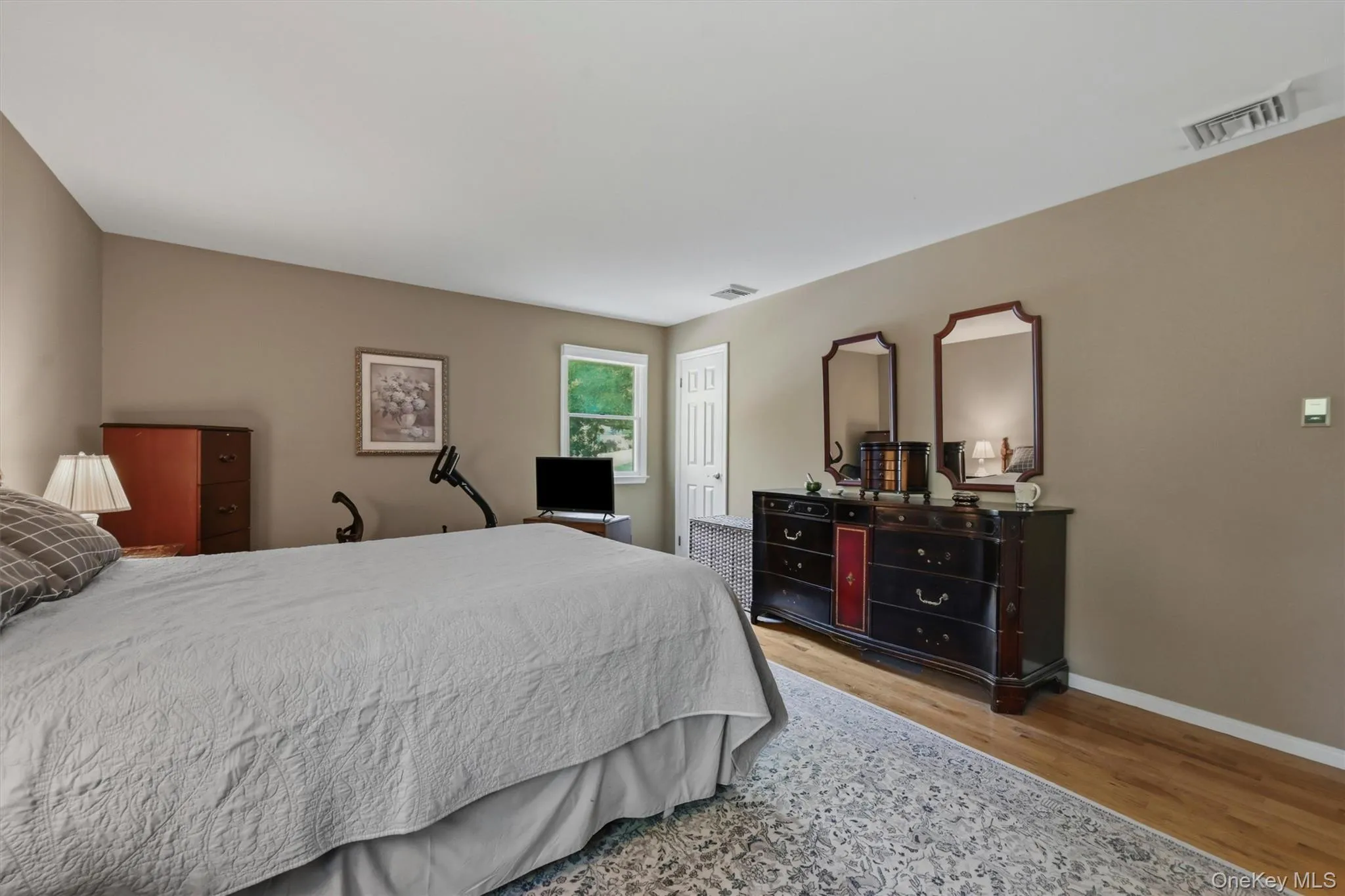 Spacious room featuring wood-finish flooring, light-toned walls, and a white ceiling Spacious room featuring wood-finish flooring, light-toned walls, and a white ceiling