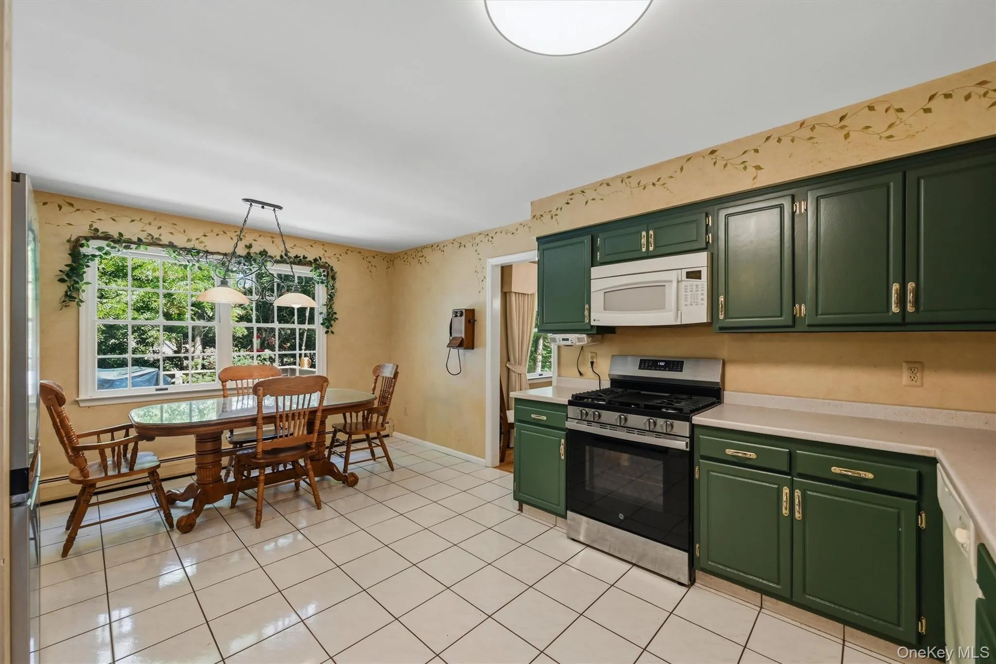 Kitchen featuring dark green cabinetry, white tile flooring, white countertops, and a full suite of appliances including a range and microwave Kitchen featuring dark green cabinetry, white tile flooring, white countertops, and a full suite of appliances including a range and microwave