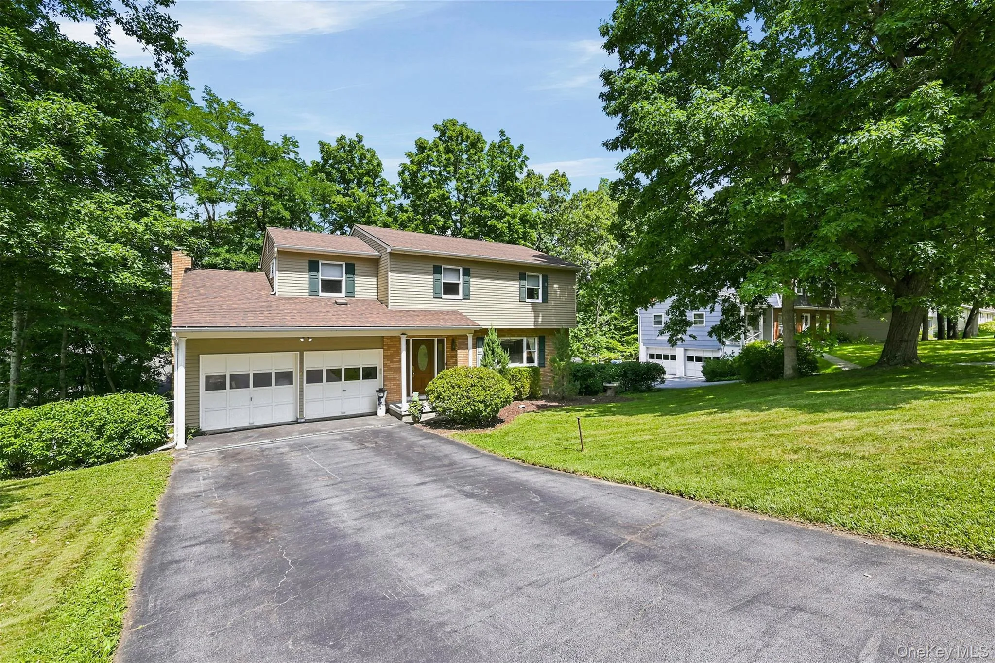 Front of residence featuring a two-car garage, asphalt driveway, and a natural wood front door with sidelights Front of residence featuring a two-car garage, asphalt driveway, and a natural wood front door with sidelights