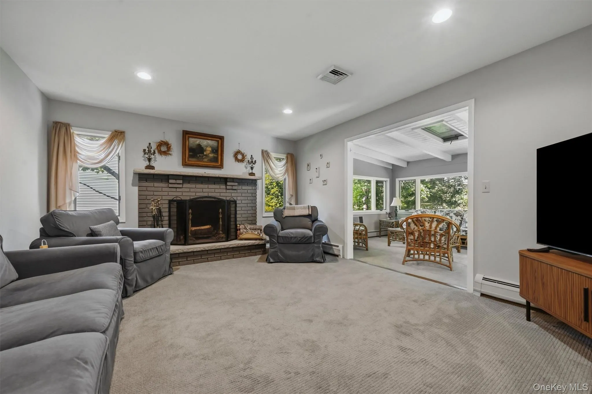 Living area featuring a brick fireplace with a stone hearth, recessed lighting, and soft gray carpeting Living area featuring a brick fireplace with a stone hearth, recessed lighting, and soft gray carpeting