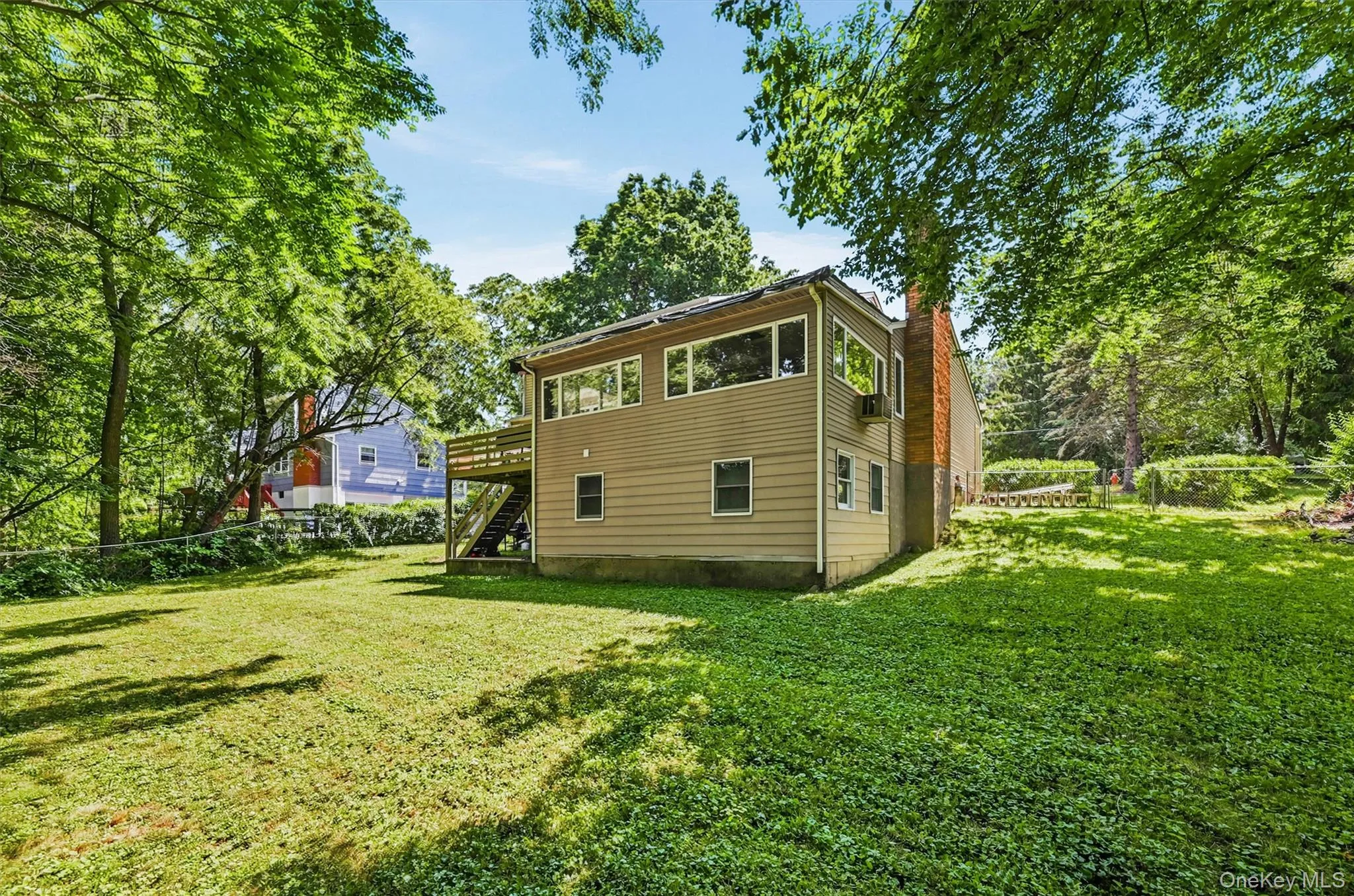 Spacious backyard featuring a two-story residence with light-colored siding, a second-story deck with stairs, a brick chimney, and abundant mature trees Spacious backyard featuring a two-story residence with light-colored siding, a second-story deck with stairs, a brick chimney, and abundant mature trees