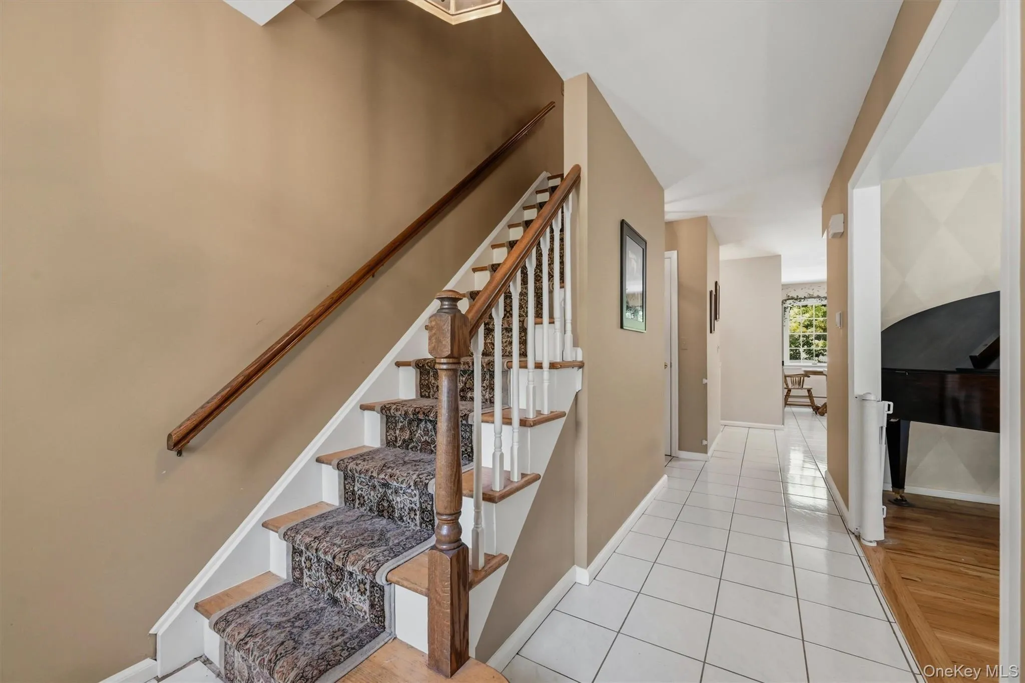 Foyer featuring a carpeted staircase with wood banister, white tile flooring, and neutral wall paint Foyer featuring a carpeted staircase with wood banister, white tile flooring, and neutral wall paint