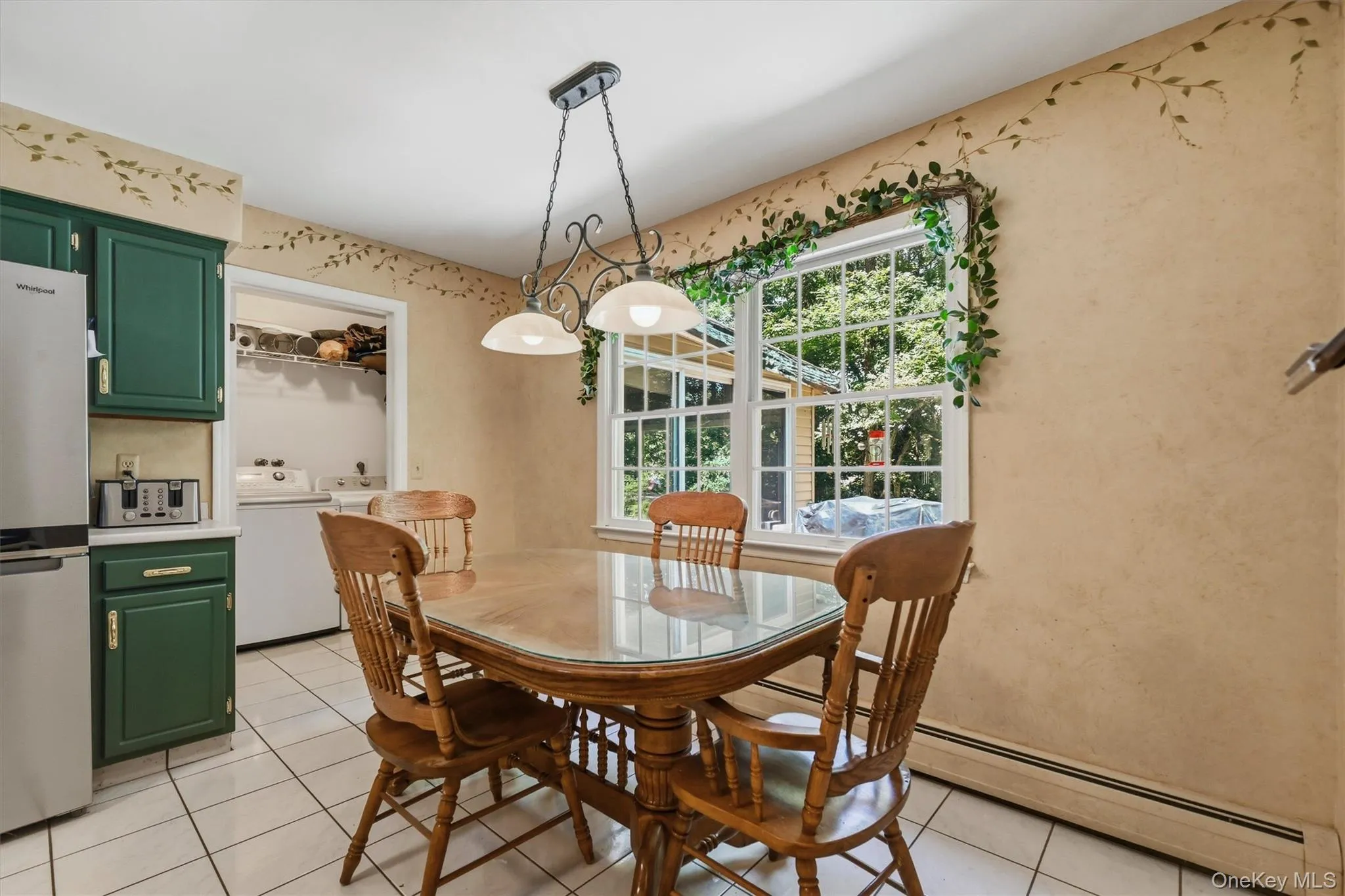 Eat-in kitchen featuring white tile flooring, green cabinetry, a stainless-steel refrigerator, and a window overlooking exterior landscaping Eat-in kitchen featuring white tile flooring, green cabinetry, a stainless-steel refrigerator, and a window overlooking exterior landscaping