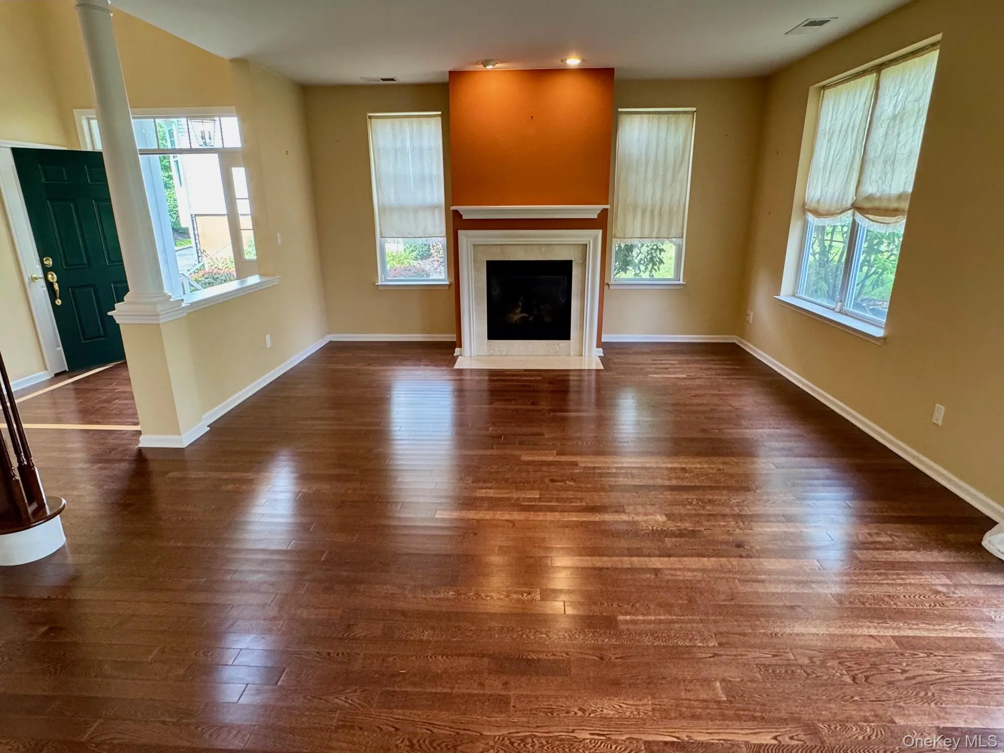 Unfurnished living room featuring dark wood-type flooring, ornate columns, and a fireplace with flush hearth Unfurnished living room featuring dark wood-type flooring, ornate columns, and a fireplace with flush hearth