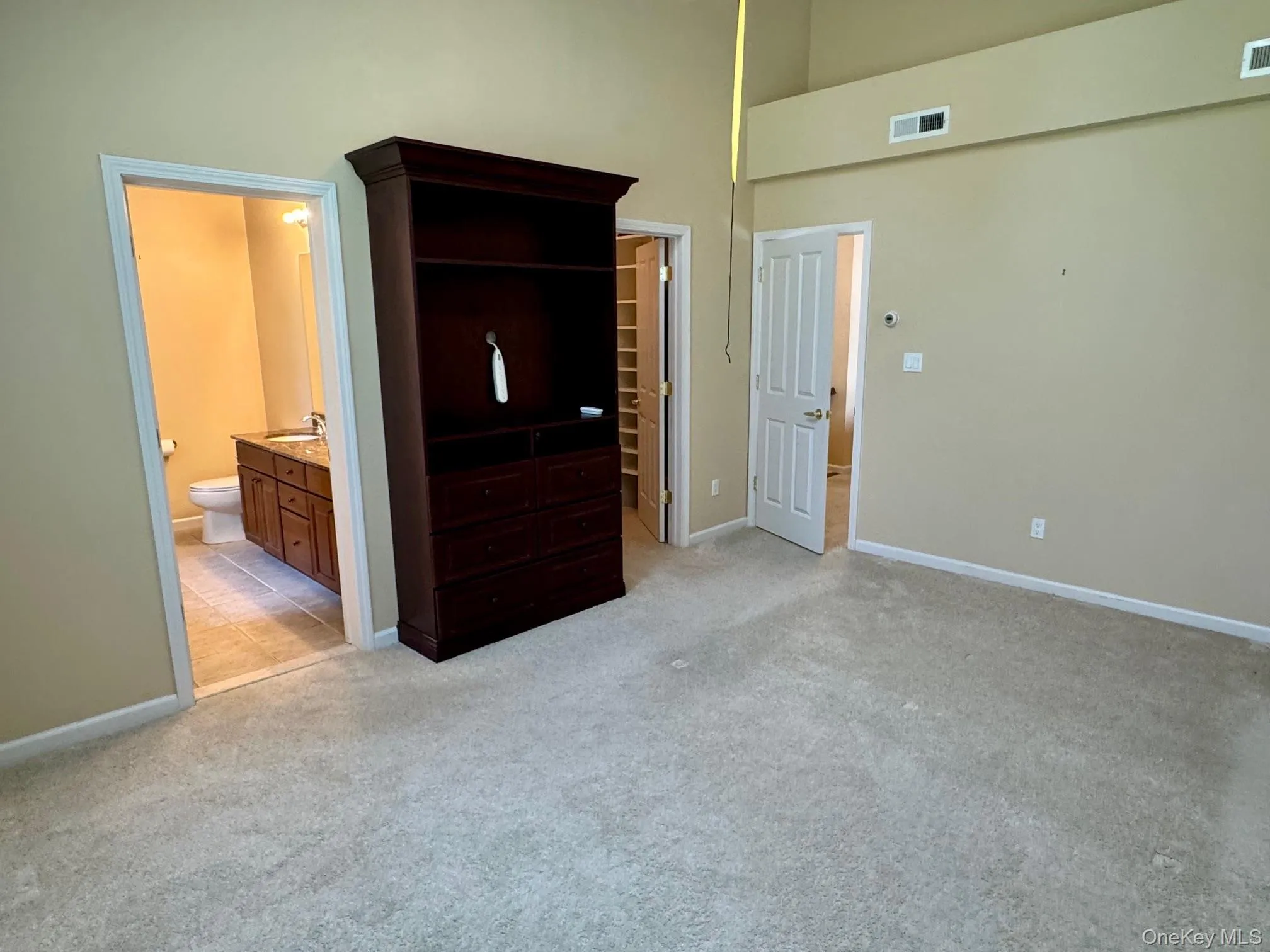 Unfurnished bedroom with a walk in closet, light colored carpet, a towering ceiling, and ensuite bath Unfurnished bedroom with a walk in closet, light colored carpet, a towering ceiling, and ensuite bath