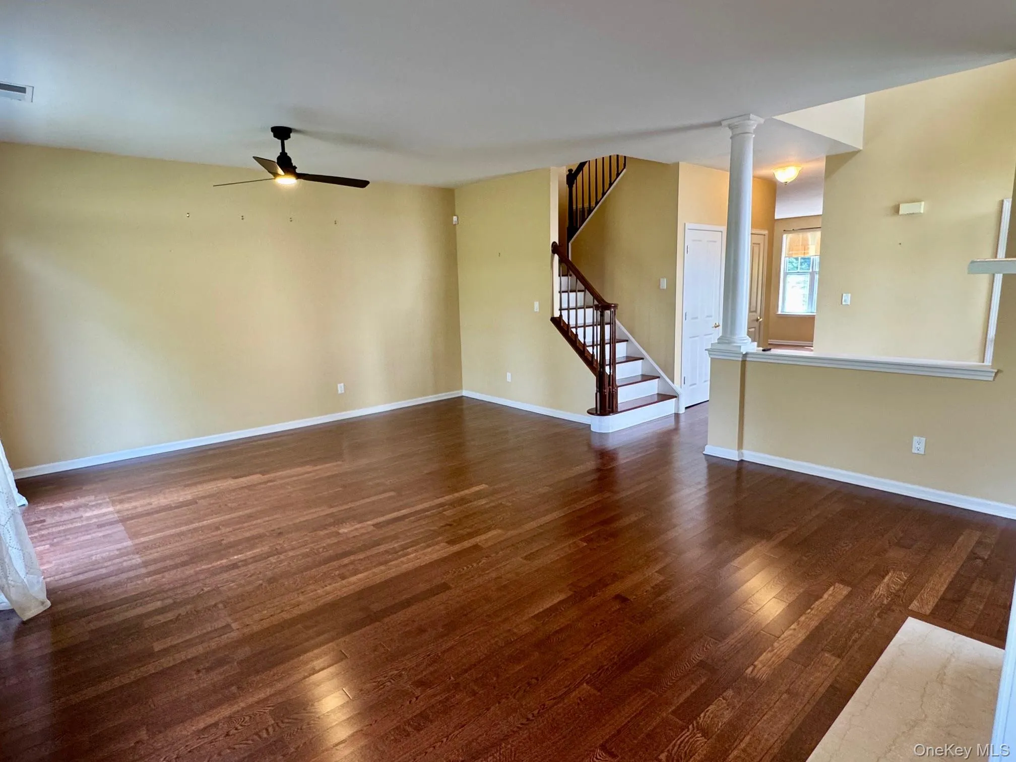Unfurnished living room with ornate columns, ceiling fan, dark wood-type flooring, and stairs Unfurnished living room with ornate columns, ceiling fan, dark wood-type flooring, and stairs