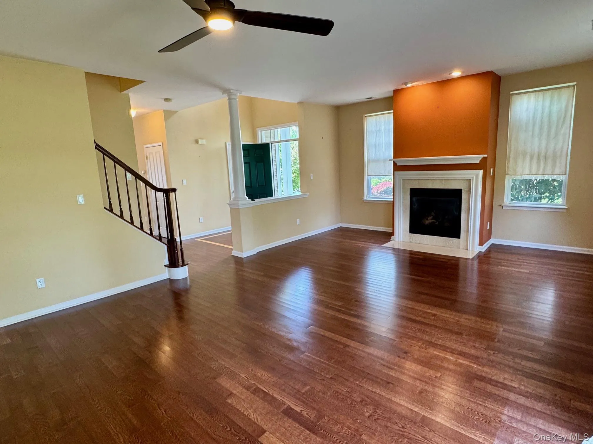 Unfurnished living room featuring ceiling fan, ornate columns, a fireplace with flush hearth, and wood finished floors Unfurnished living room featuring ceiling fan, ornate columns, a fireplace with flush hearth, and wood finished floors