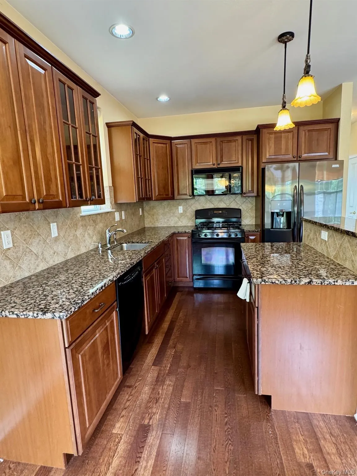 Kitchen featuring black appliances, dark wood-style floors, dark stone counters, backsplash, and recessed lighting Kitchen featuring black appliances, dark wood-style floors, dark stone counters, backsplash, and recessed lighting