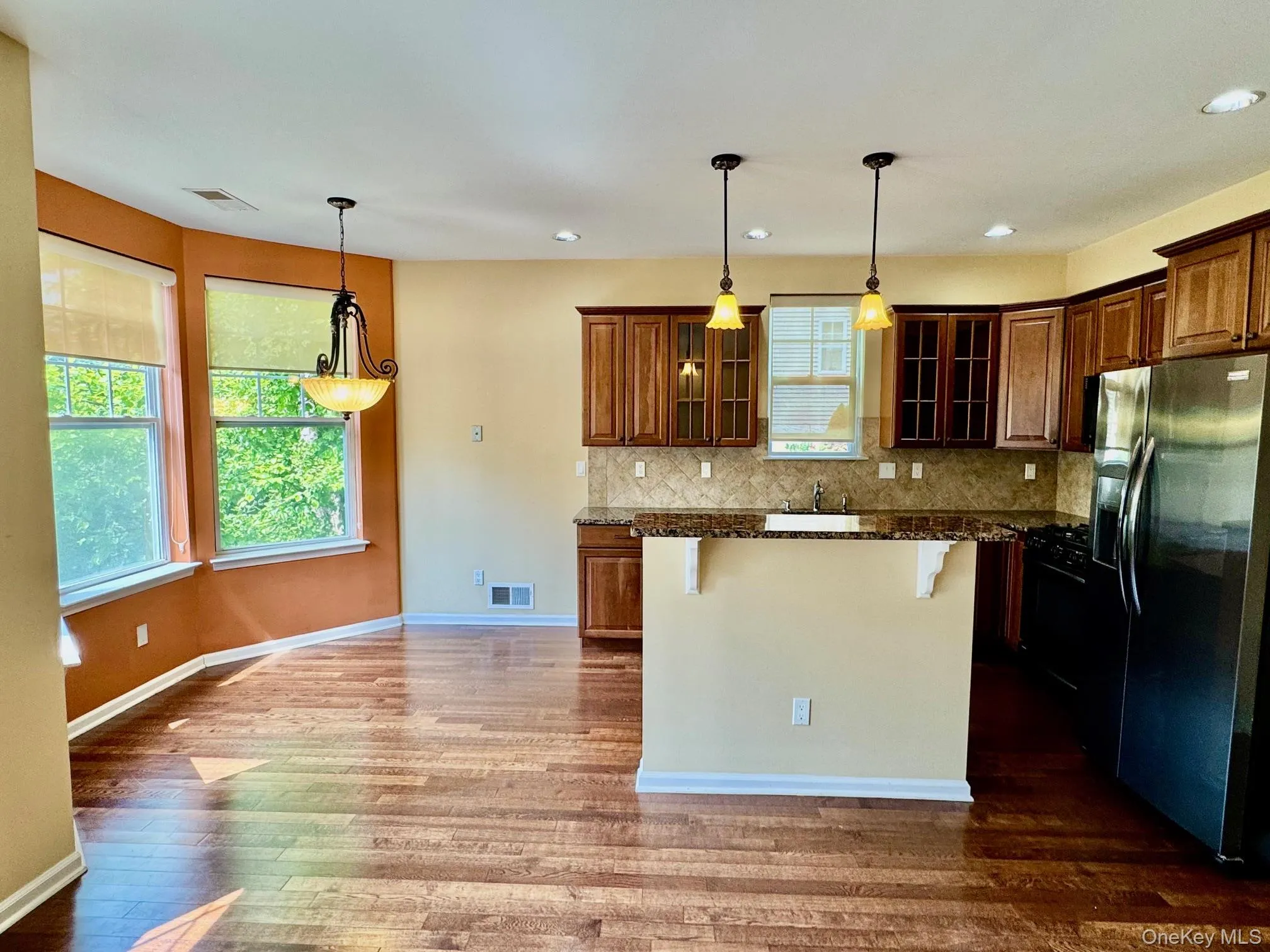 Kitchen with refrigerator with ice dispenser, a kitchen breakfast bar, dark wood-style flooring, decorative backsplash, and glass insert cabinets Kitchen with refrigerator with ice dispenser, a kitchen breakfast bar, dark wood-style flooring, decorative backsplash, and glass insert cabinets