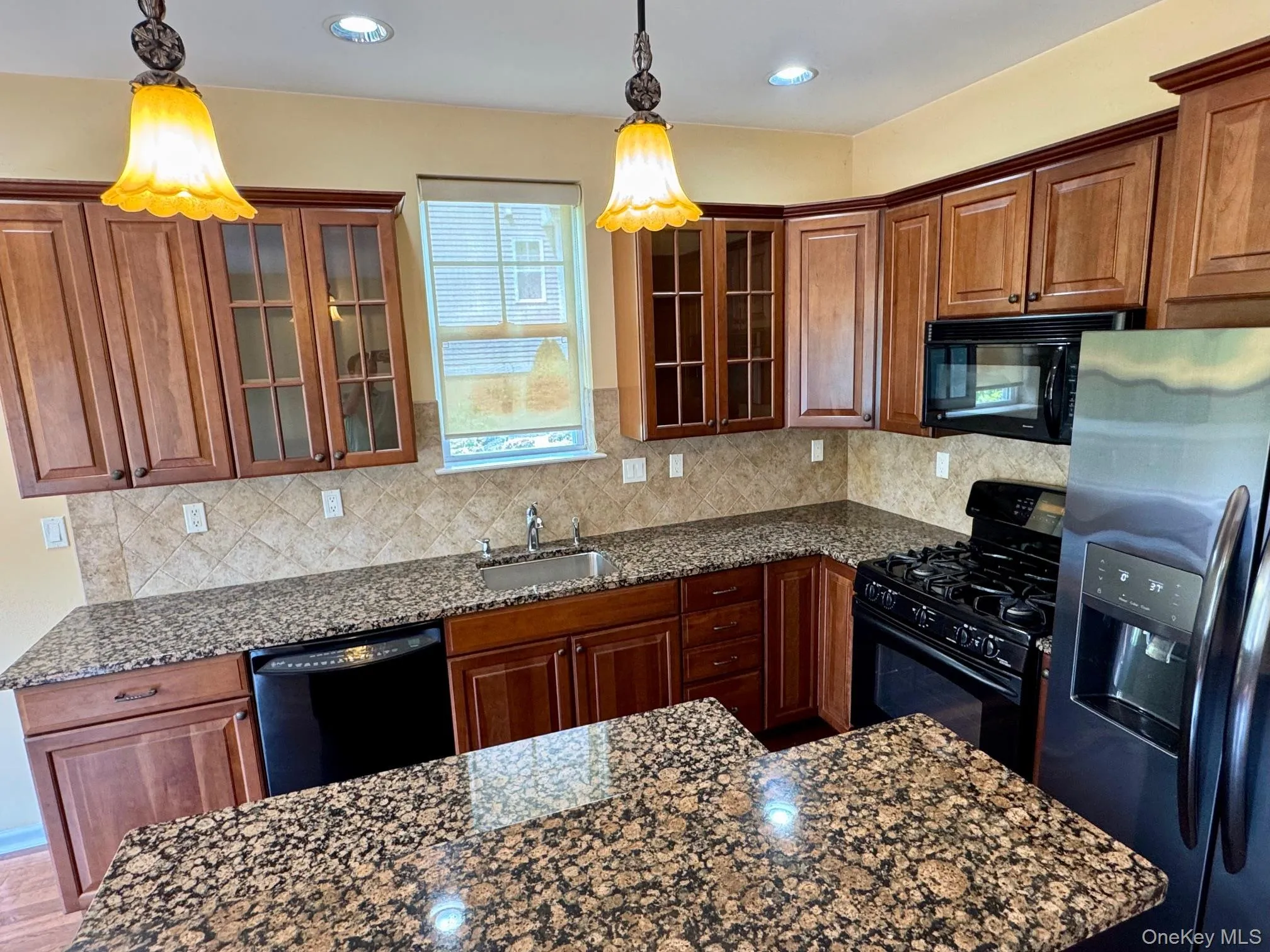 Kitchen with black appliances, glass insert cabinets, dark stone counters, tasteful backsplash, and recessed lighting Kitchen with black appliances, glass insert cabinets, dark stone counters, tasteful backsplash, and recessed lighting