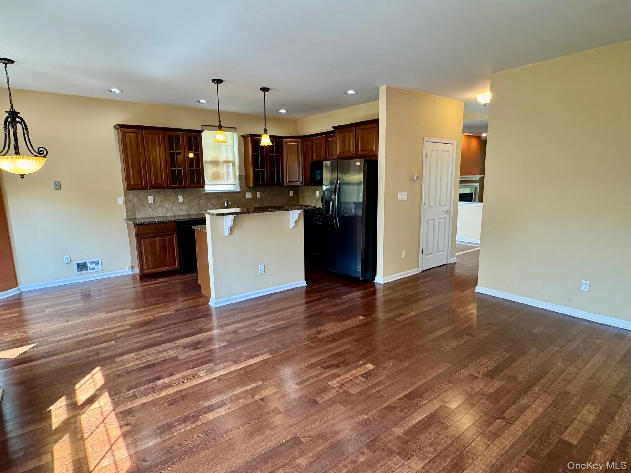 Kitchen featuring fridge with ice dispenser, a center island, backsplash, glass insert cabinets, and dark wood-type flooring Kitchen featuring fridge with ice dispenser, a center island, backsplash, glass insert cabinets, and dark wood-type flooring