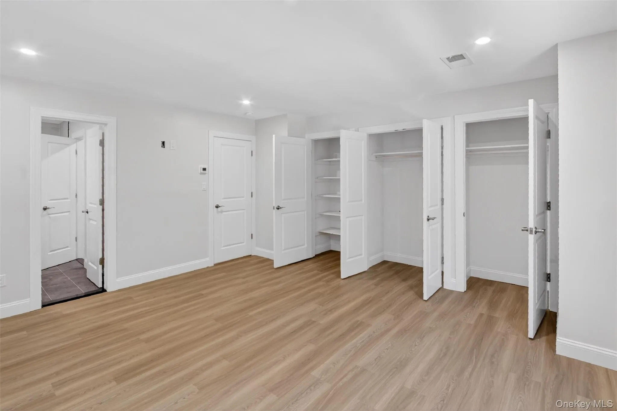Spacious room featuring wood-finish flooring, recessed lighting, and multiple white panel doors Spacious room featuring wood-finish flooring, recessed lighting, and multiple white panel doors