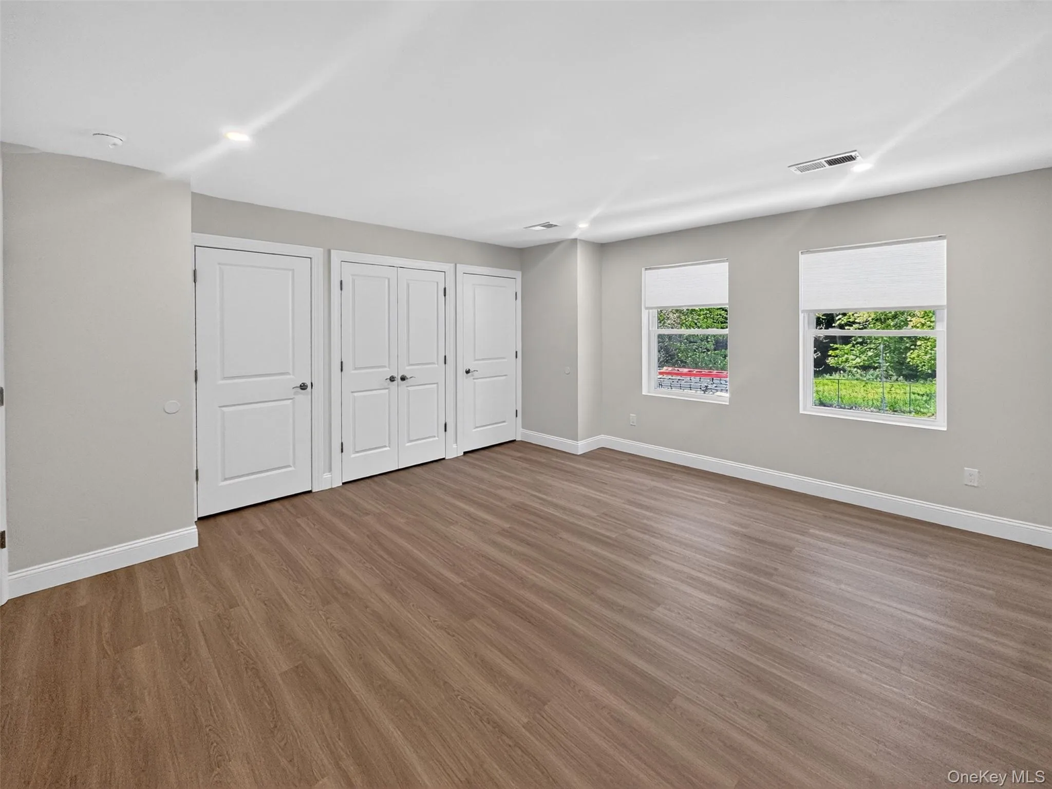 Spacious interior featuring wood-finish flooring, recessed lighting, and multiple white panel doors Spacious interior featuring wood-finish flooring, recessed lighting, and multiple white panel doors