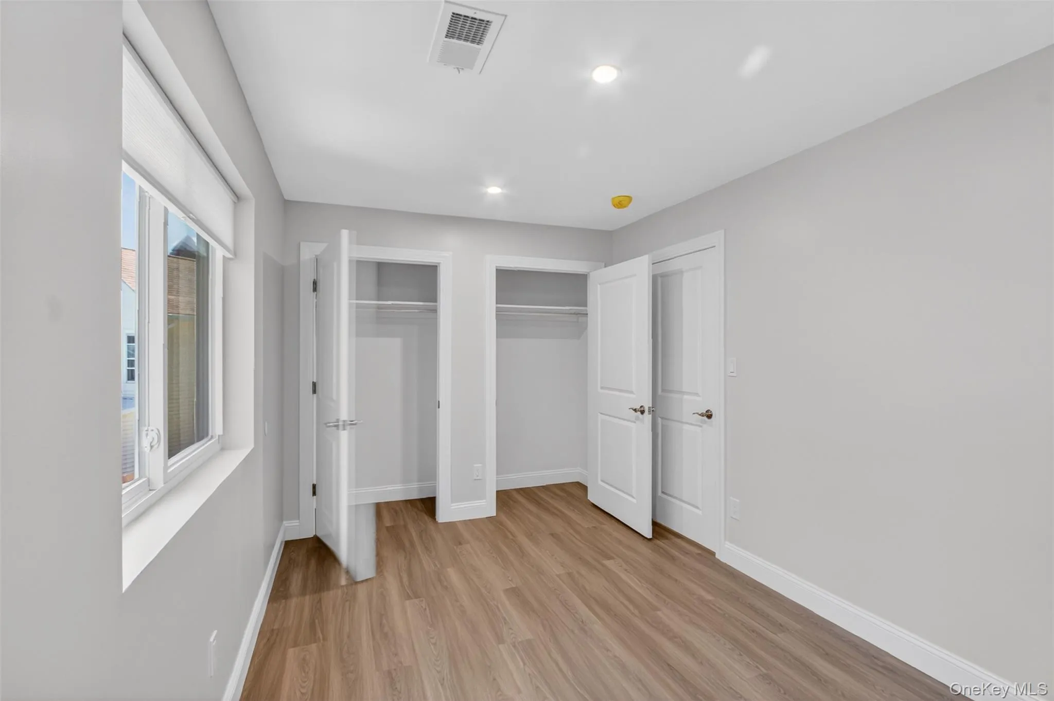 Room featuring wood-finish flooring, light grey painted walls, and a white window blind Room featuring wood-finish flooring, light grey painted walls, and a white window blind