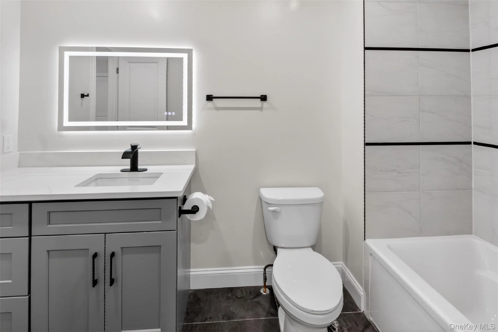 Contemporary bathroom featuring a grey vanity with a white countertop and rectangular sink, matte black faucet, and an illuminated mirrored cabinet Contemporary bathroom featuring a grey vanity with a white countertop and rectangular sink, matte black faucet, and an illuminated mirrored cabinet