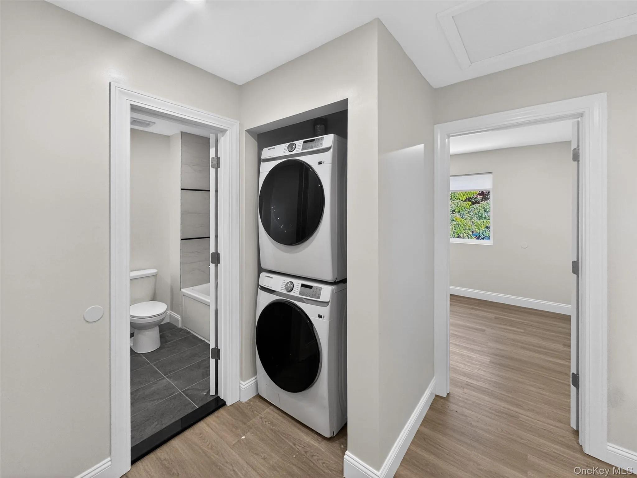 Dedicated laundry closet featuring a stacked washer and dryer, wood-finish flooring, and crisp white trim Dedicated laundry closet featuring a stacked washer and dryer, wood-finish flooring, and crisp white trim