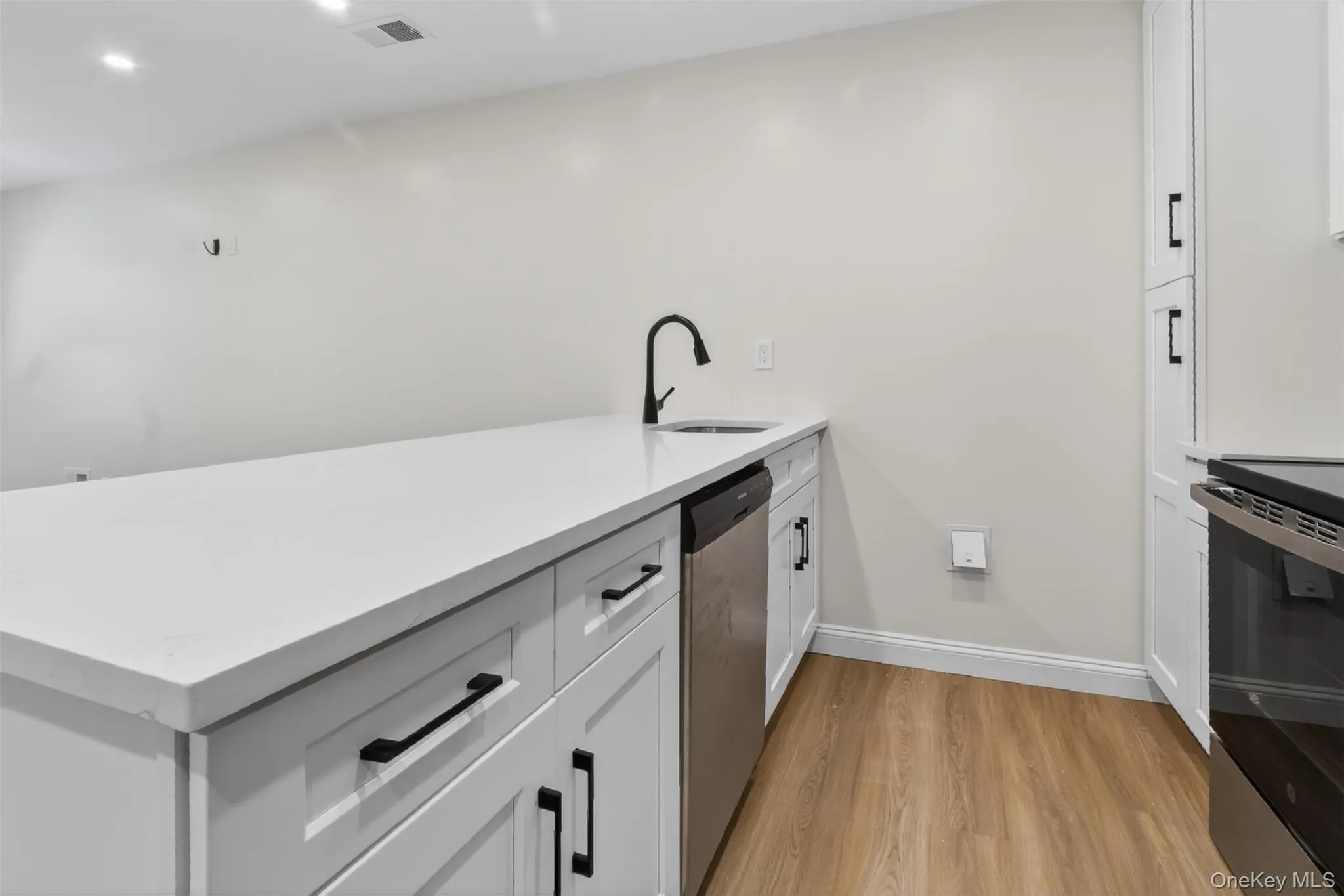 Kitchen island featuring a white countertop, undermount sink with a black gooseneck faucet, and integrated stainless steel dishwasher Kitchen island featuring a white countertop, undermount sink with a black gooseneck faucet, and integrated stainless steel dishwasher