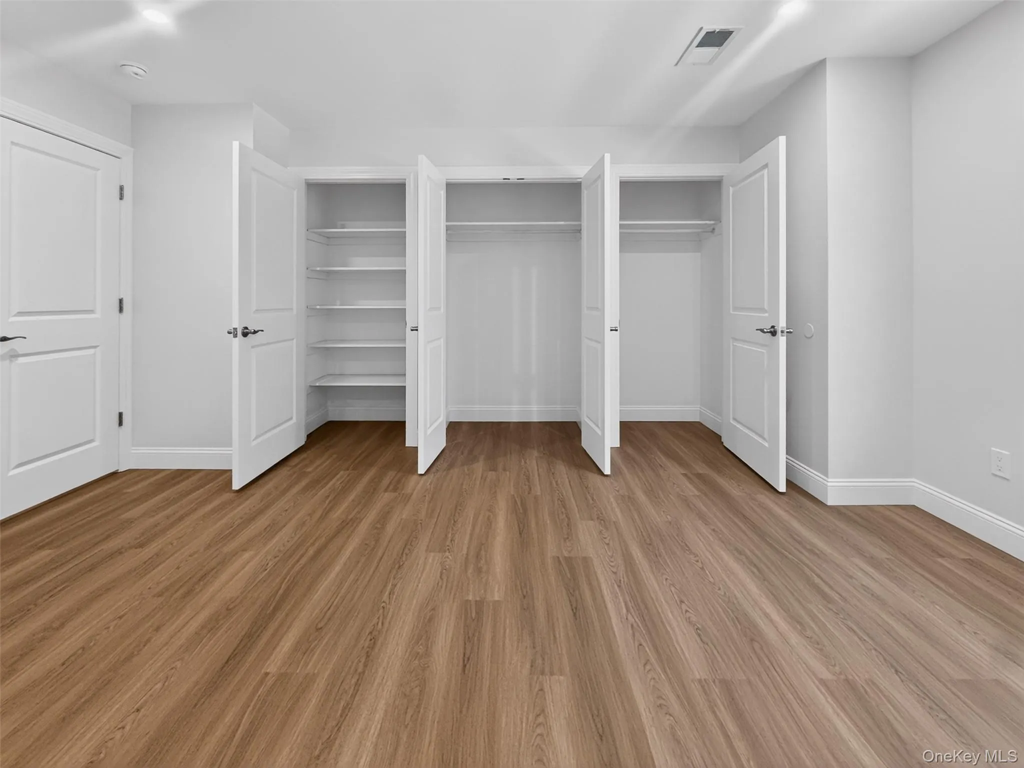 Bright room featuring wood-finish flooring, white walls, and white baseboards Bright room featuring wood-finish flooring, white walls, and white baseboards