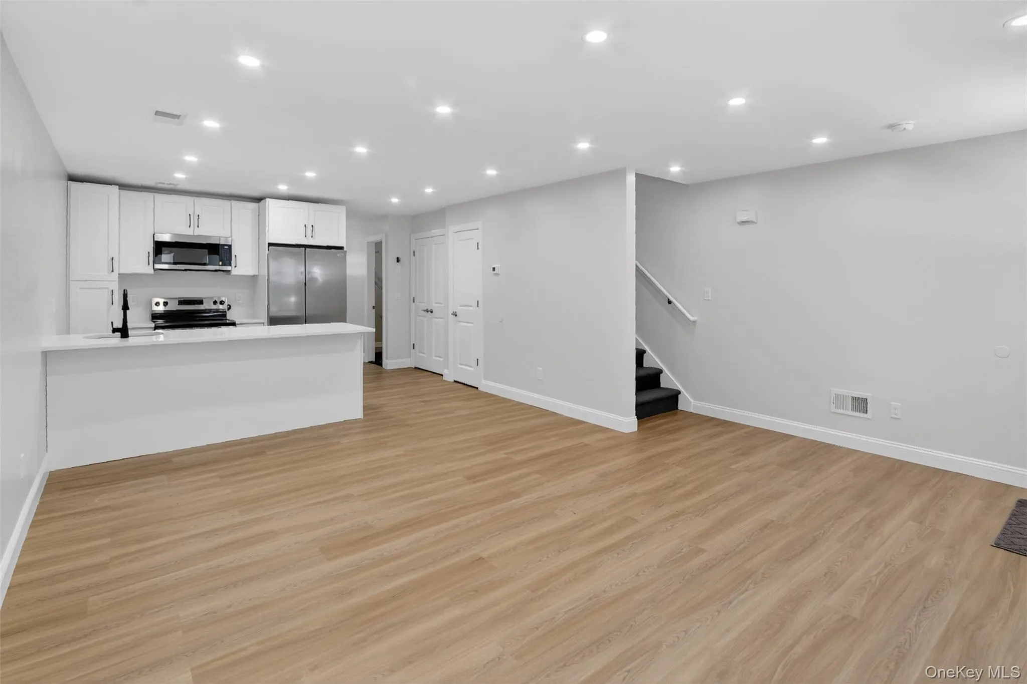 Open-concept living space featuring a modern kitchen with white cabinetry, stainless steel appliances, and a breakfast bar Open-concept living space featuring a modern kitchen with white cabinetry, stainless steel appliances, and a breakfast bar