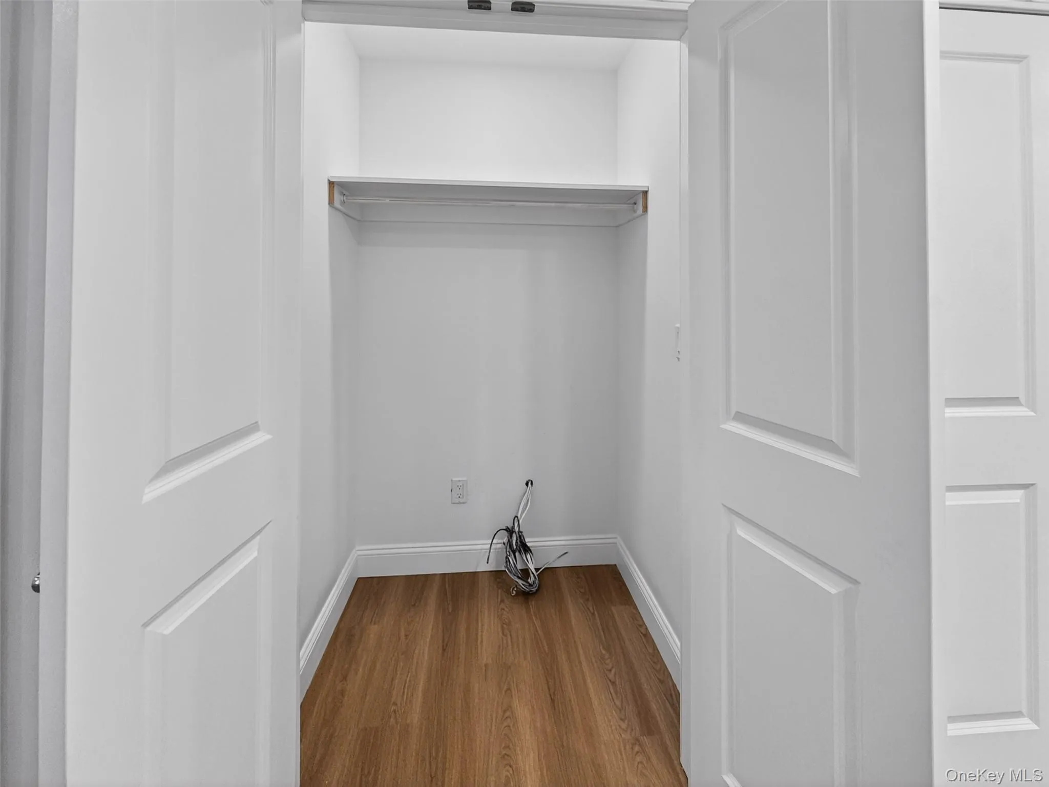 Interior closet with wood-finish flooring, white walls, and a built-in shelf with a hanging rod Interior closet with wood-finish flooring, white walls, and a built-in shelf with a hanging rod