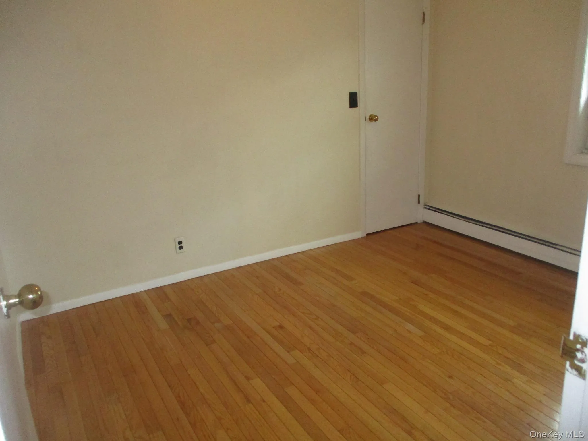 Empty room with baseboard heating, light wood finished floors, and baseboards Empty room with baseboard heating, light wood finished floors, and baseboards