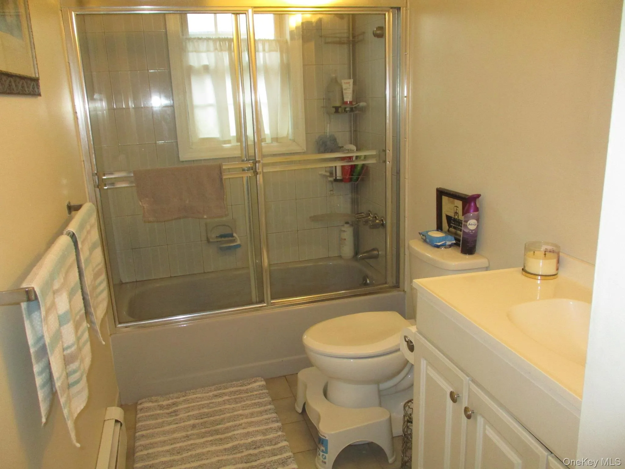 Bathroom featuring vanity, a baseboard heating unit, enclosed tub / shower combo, tile patterned flooring, and toilet Bathroom featuring vanity, a baseboard heating unit, enclosed tub / shower combo, tile patterned flooring, and toilet