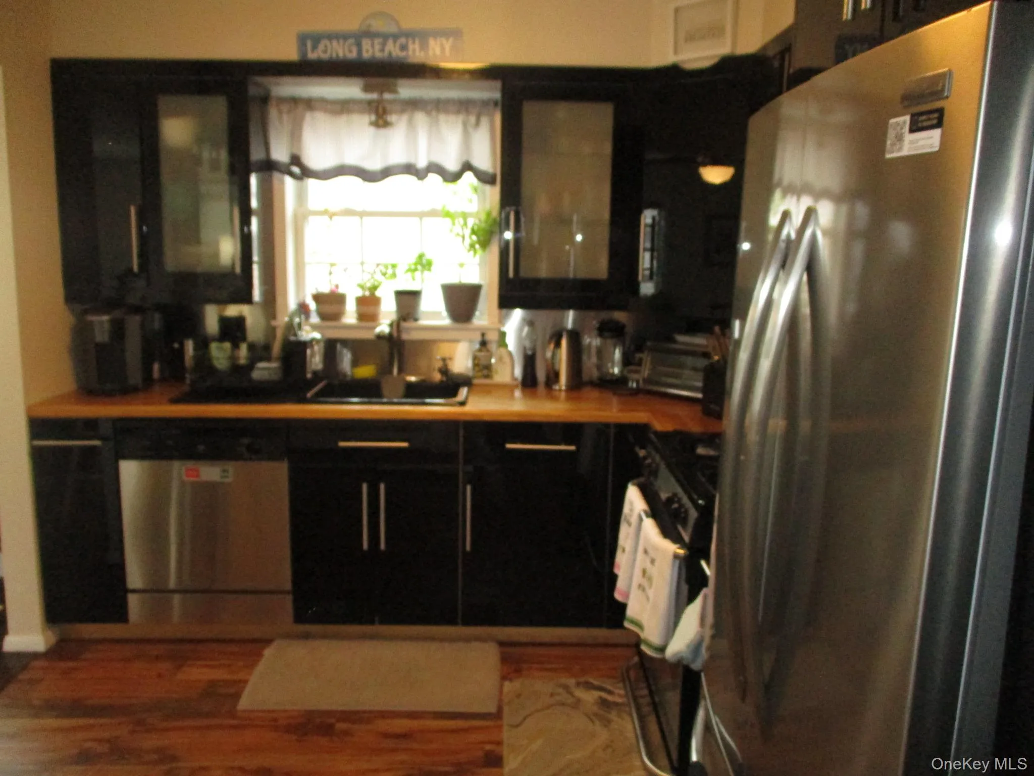 Kitchen with glass insert cabinets, appliances with stainless steel finishes, wood finished floors, a sink, and dark cabinetry Kitchen with glass insert cabinets, appliances with stainless steel finishes, wood finished floors, a sink, and dark cabinetry