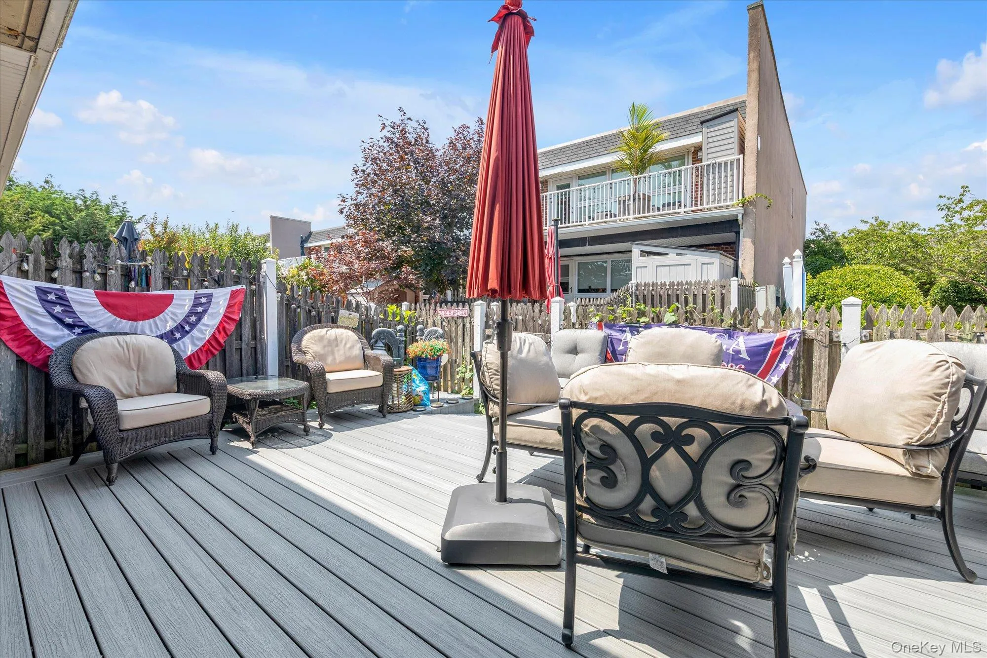 Spacious outdoor deck featuring composite decking, a wooden privacy fence, and an upper-level balcony Spacious outdoor deck featuring composite decking, a wooden privacy fence, and an upper-level balcony