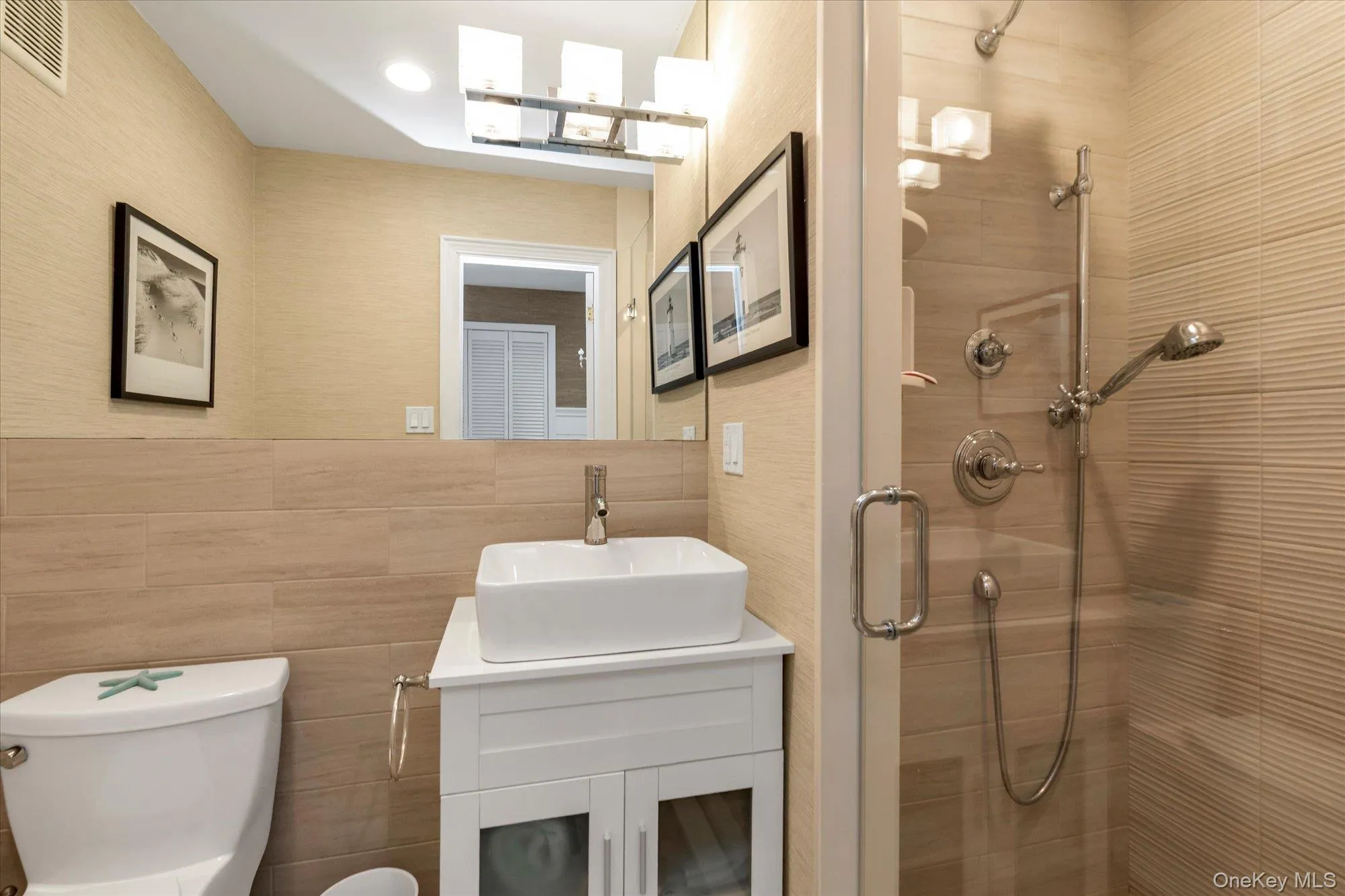 Contemporary second bathroom featuring a glass-enclosed shower with multiple shower heads, a sleek vessel sink set atop a white vanity, a full-width mirror, and horizontally-aligned wall tiling Contemporary second bathroom featuring a glass-enclosed shower with multiple shower heads, a sleek vessel sink set atop a white vanity, a full-width mirror, and horizontally-aligned wall tiling