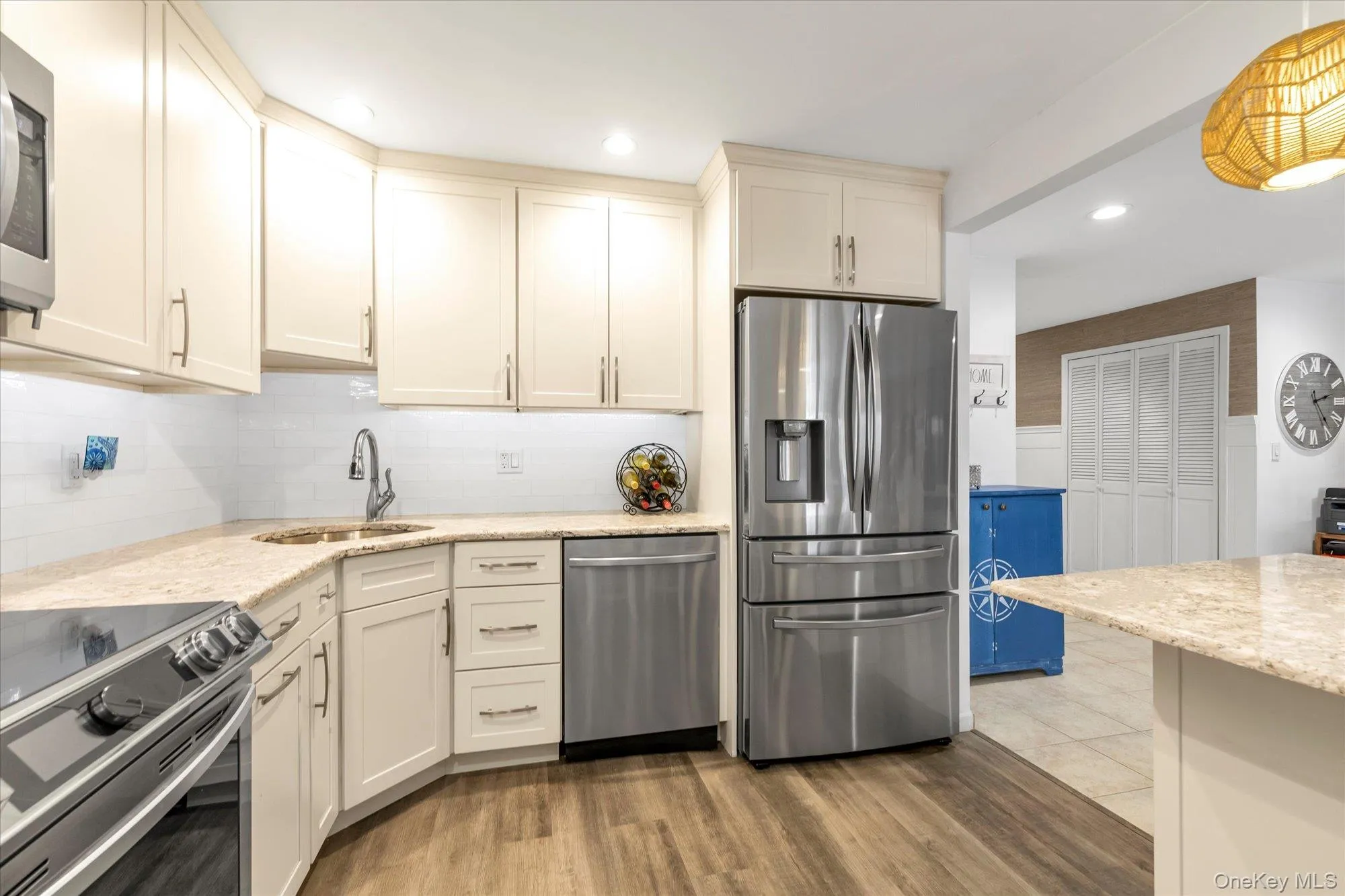 Kitchen featuring cream-colored cabinetry, stainless steel appliances, speckled countertops, a subway tile backsplash, and wood-finish flooring Kitchen featuring cream-colored cabinetry, stainless steel appliances, speckled countertops, a subway tile backsplash, and wood-finish flooring