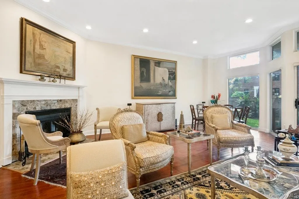 Recessed lighting illuminates the living area with hardwood flooring, a fireplace featuring a stone surround, and an expansive window Recessed lighting illuminates the living area with hardwood flooring, a fireplace featuring a stone surround, and an expansive window