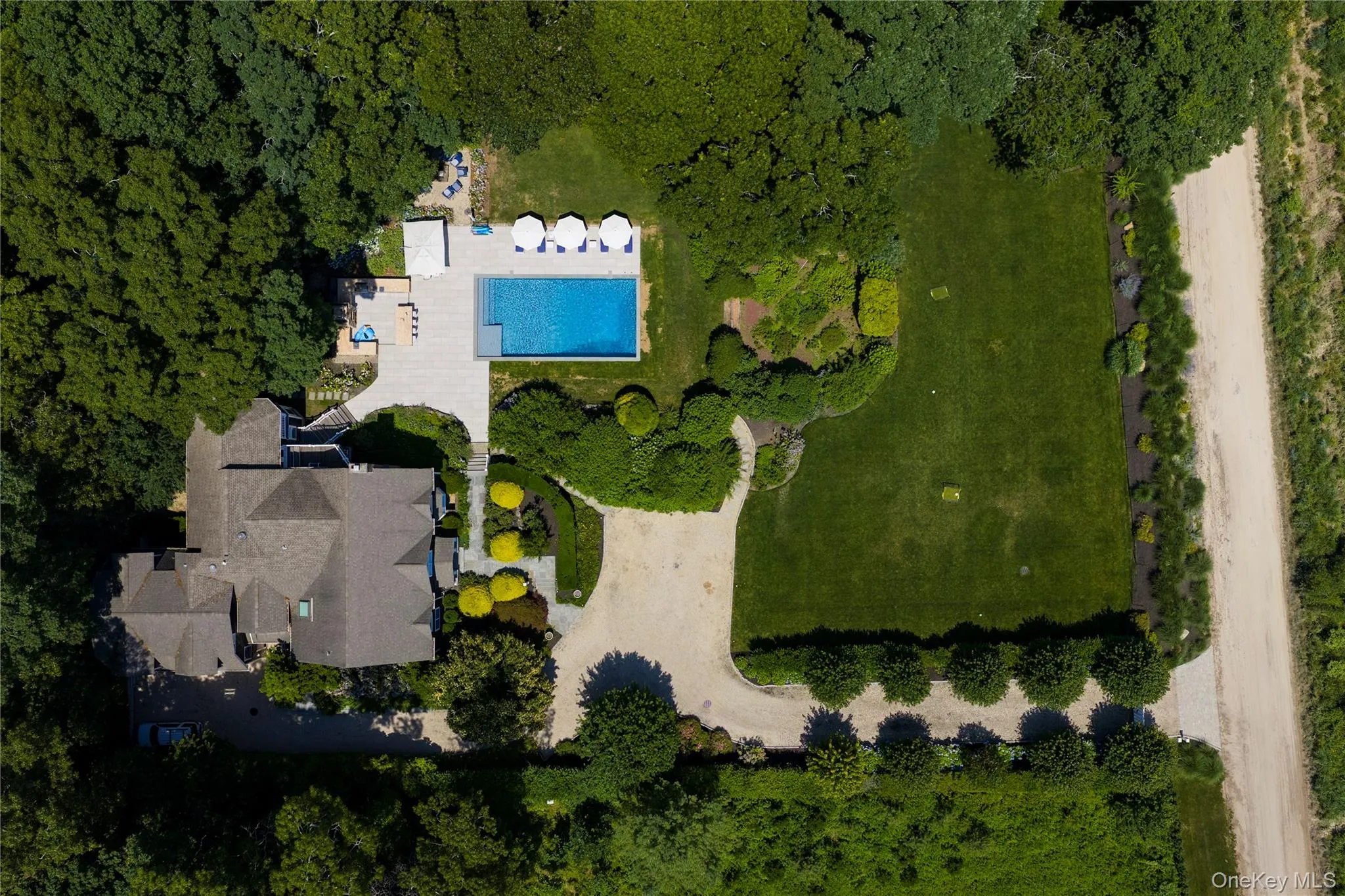 Expansive property featuring a large residence with a multi-gabled roofline, a rectangular swimming pool, and a gravel driveway Expansive property featuring a large residence with a multi-gabled roofline, a rectangular swimming pool, and a gravel driveway