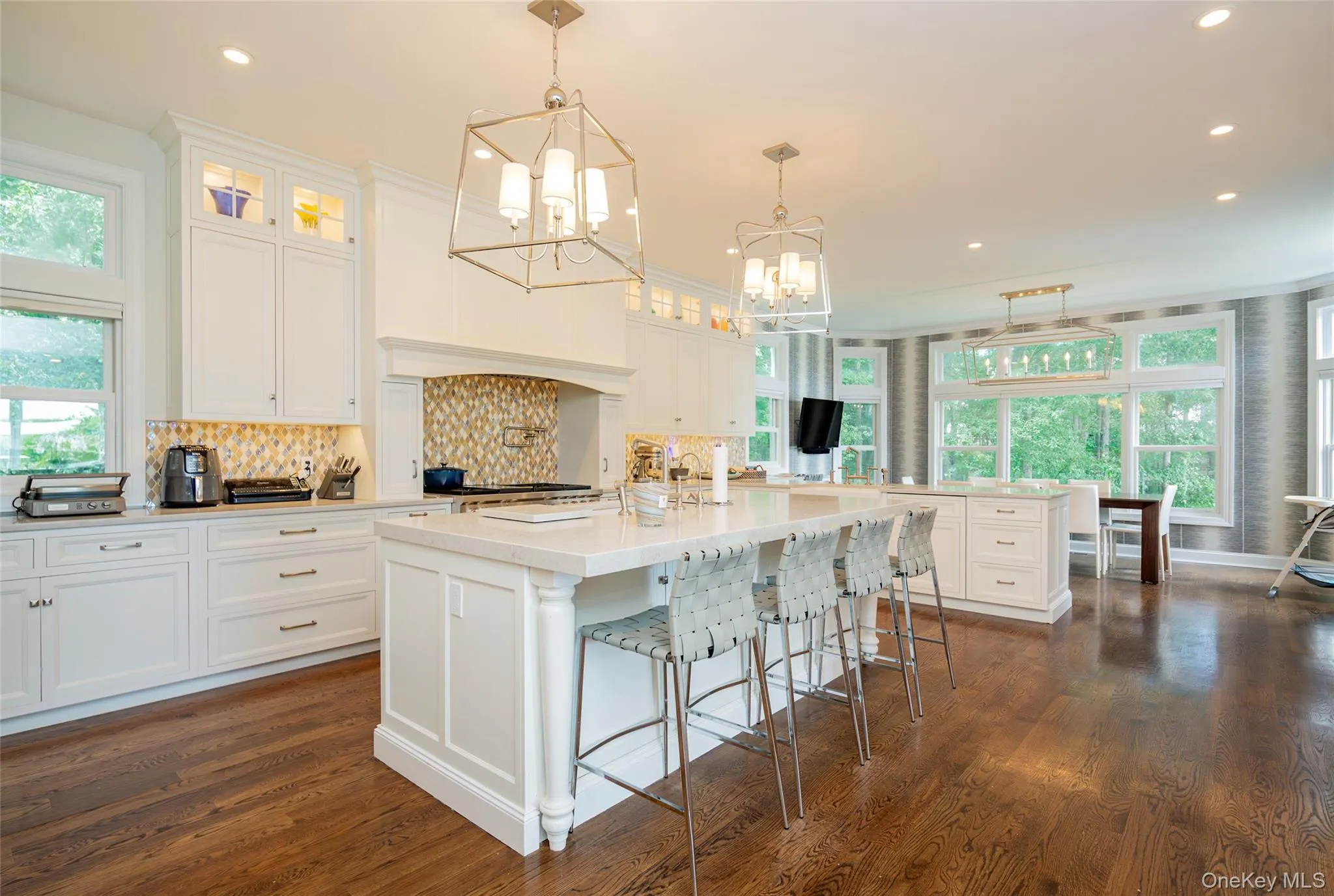 Spacious kitchen featuring white cabinetry, a large center island with seating, dark wood-finish flooring, and multiple windows Spacious kitchen featuring white cabinetry, a large center island with seating, dark wood-finish flooring, and multiple windows
