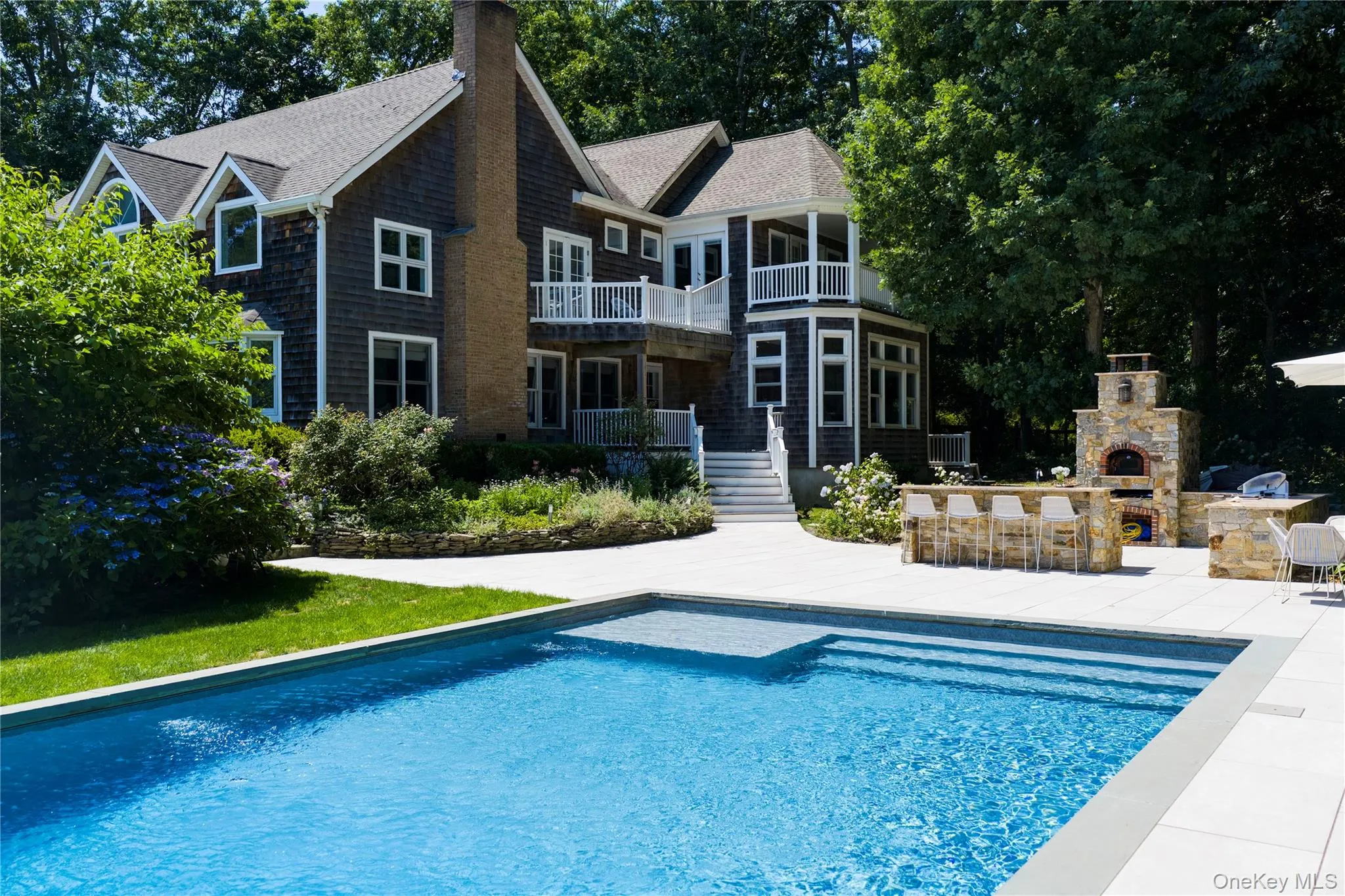In-ground swimming pool with integrated steps and sun shelf, expansive patio, and an outdoor kitchen featuring a built-in pizza oven In-ground swimming pool with integrated steps and sun shelf, expansive patio, and an outdoor kitchen featuring a built-in pizza oven