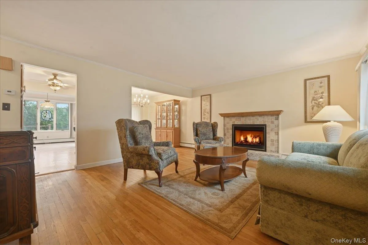 Living area featuring wood-finish flooring, a tiled fireplace with a wood mantel, and crown molding Living area featuring wood-finish flooring, a tiled fireplace with a wood mantel, and crown molding