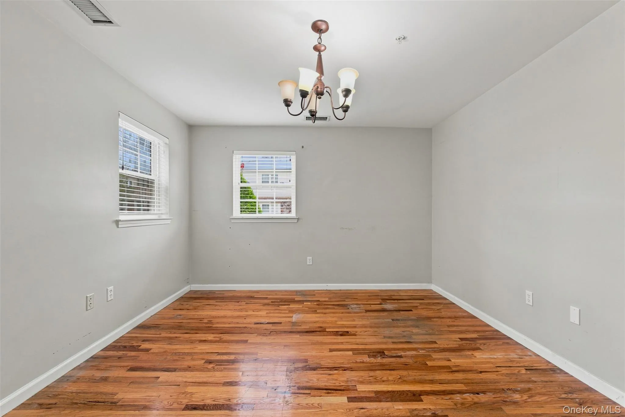 Spacious room featuring rich wood-finish flooring, light gray wall tones, and white trim Spacious room featuring rich wood-finish flooring, light gray wall tones, and white trim
