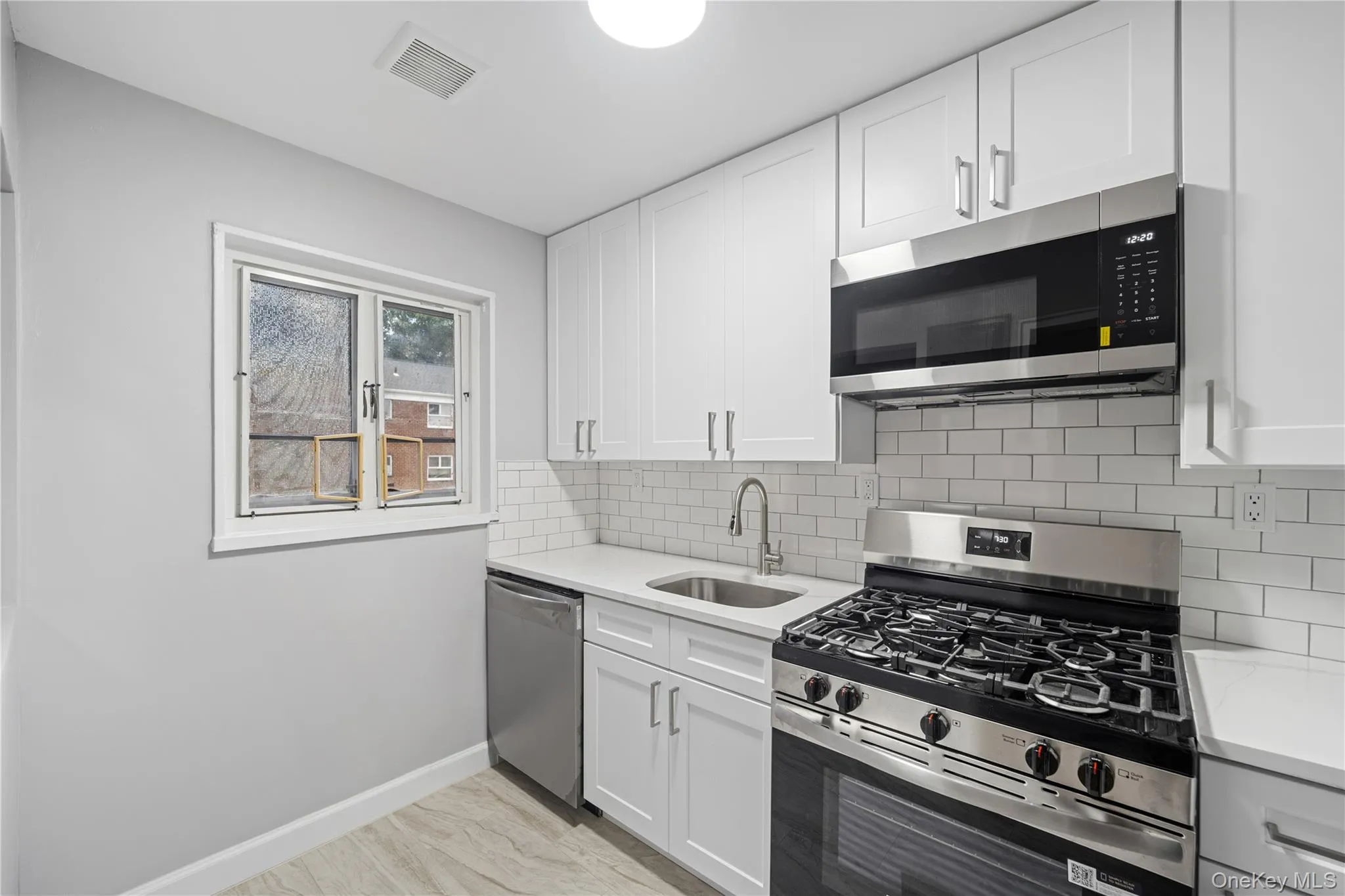 Kitchen featuring white shaker cabinetry, stainless steel appliances, light-toned countertops, subway tile backsplash, and light wood-finish flooring Kitchen featuring white shaker cabinetry, stainless steel appliances, light-toned countertops, subway tile backsplash, and light wood-finish flooring