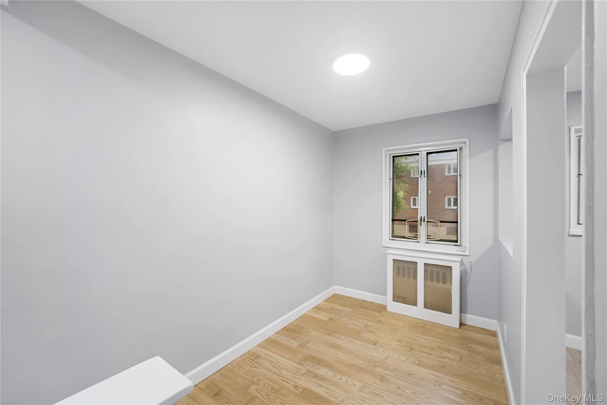 Room featuring light wood-finish flooring, a white window frame, and a white radiator cover Room featuring light wood-finish flooring, a white window frame, and a white radiator cover